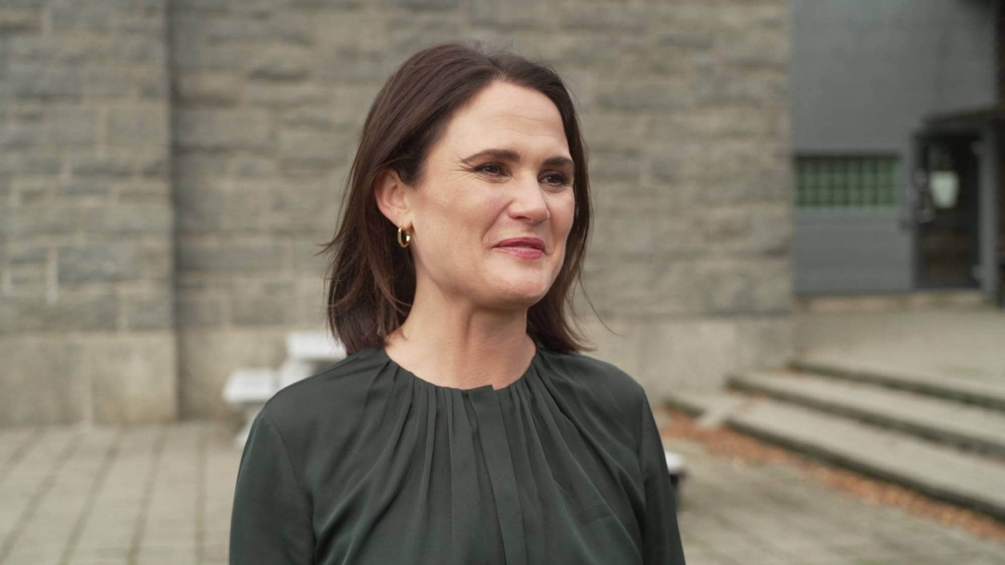 Ingrid Schjerven Smedsrud står utendørs foran en grå steinvegg. (Bildebeskrivelsen er laget av en KI-tjeneste)