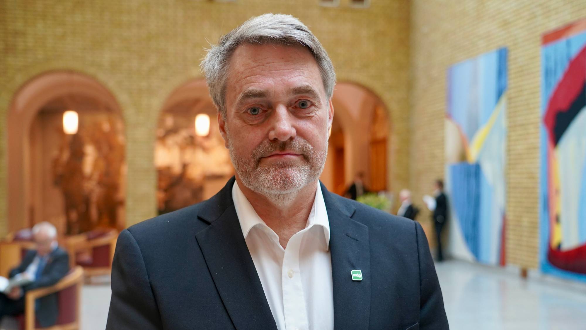 Mann med mørkt hår, hvit skjorte og dressjakke ser i kamera