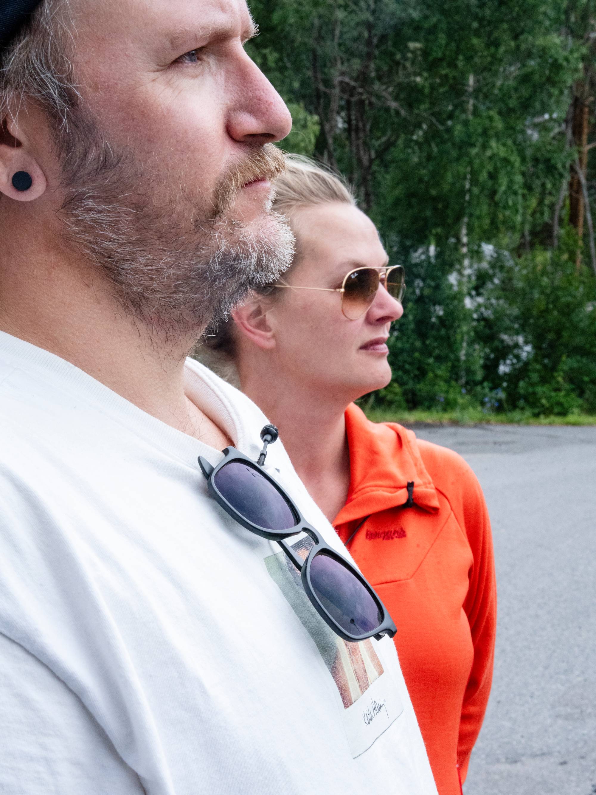 En mann og en kvinne står ved siden av hverandre utendørs. Begge ser i samme retning. (Bildebeskrivelsen er laget av en KI-tjeneste)