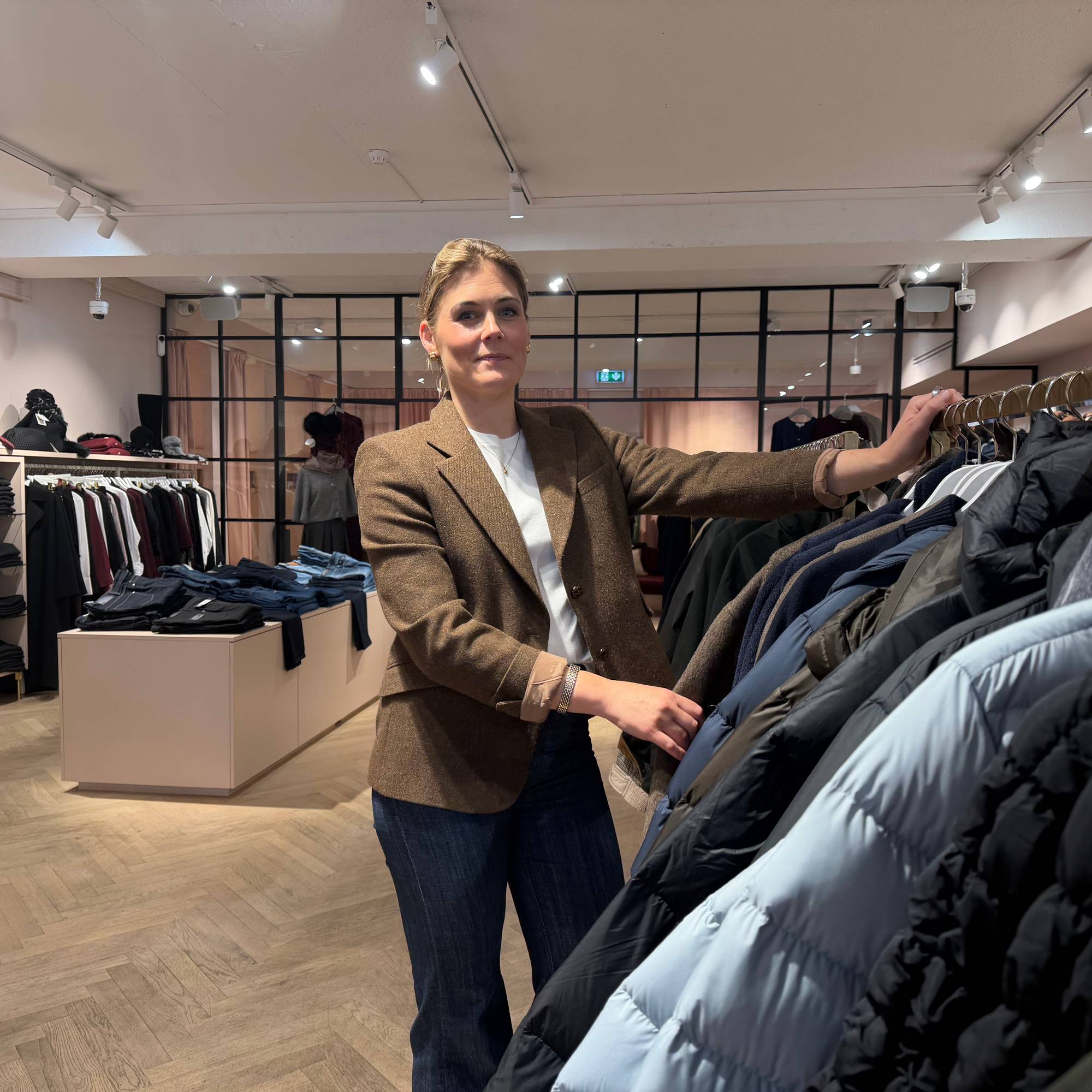 Eier og driver Tini Flaat Mykland i T.Lynn står ved klesstativ med butikken sin i bakgrunnen. 