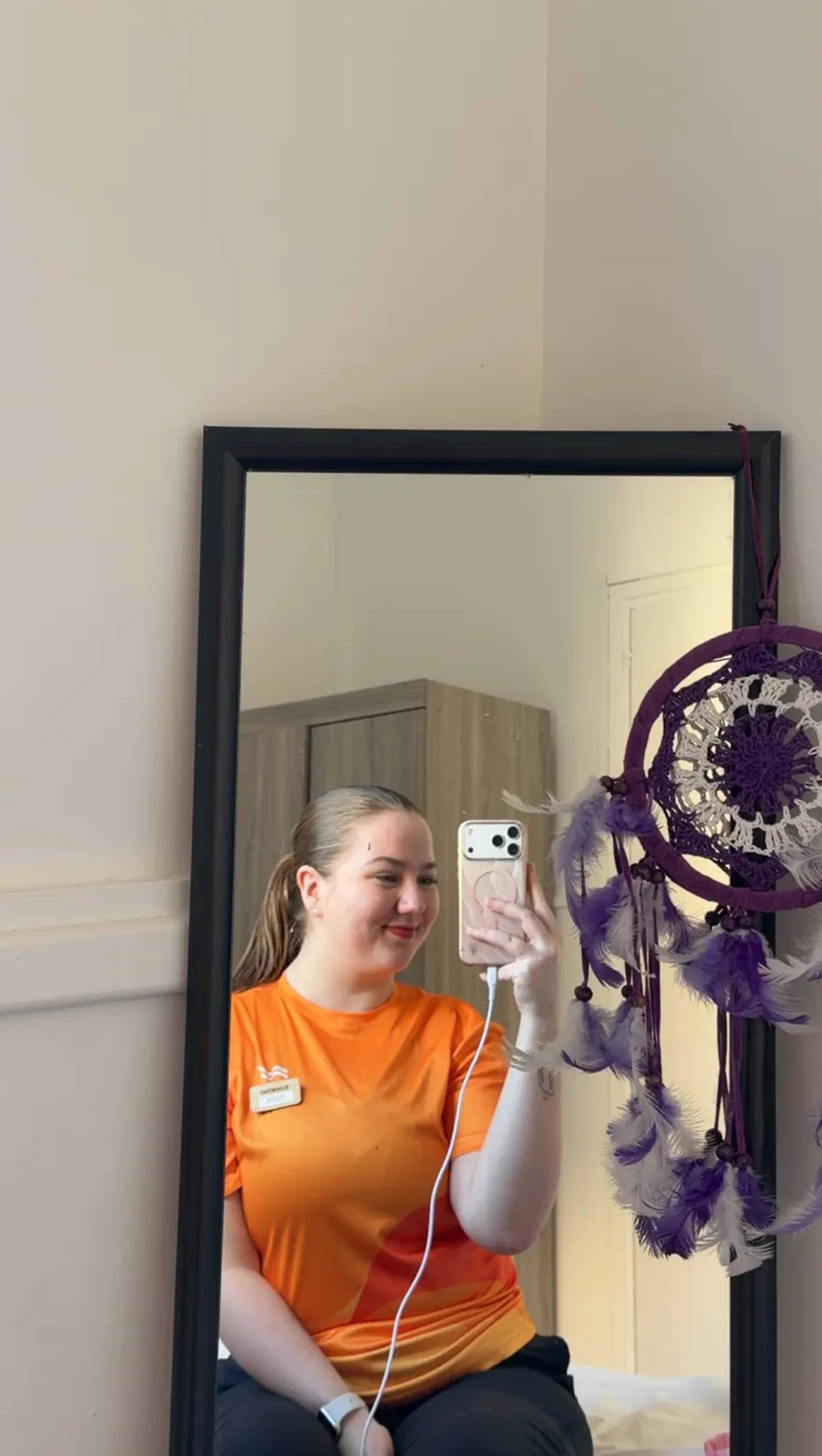 Speilbilde av av ei jente med oransje t-skjorte og hestehale