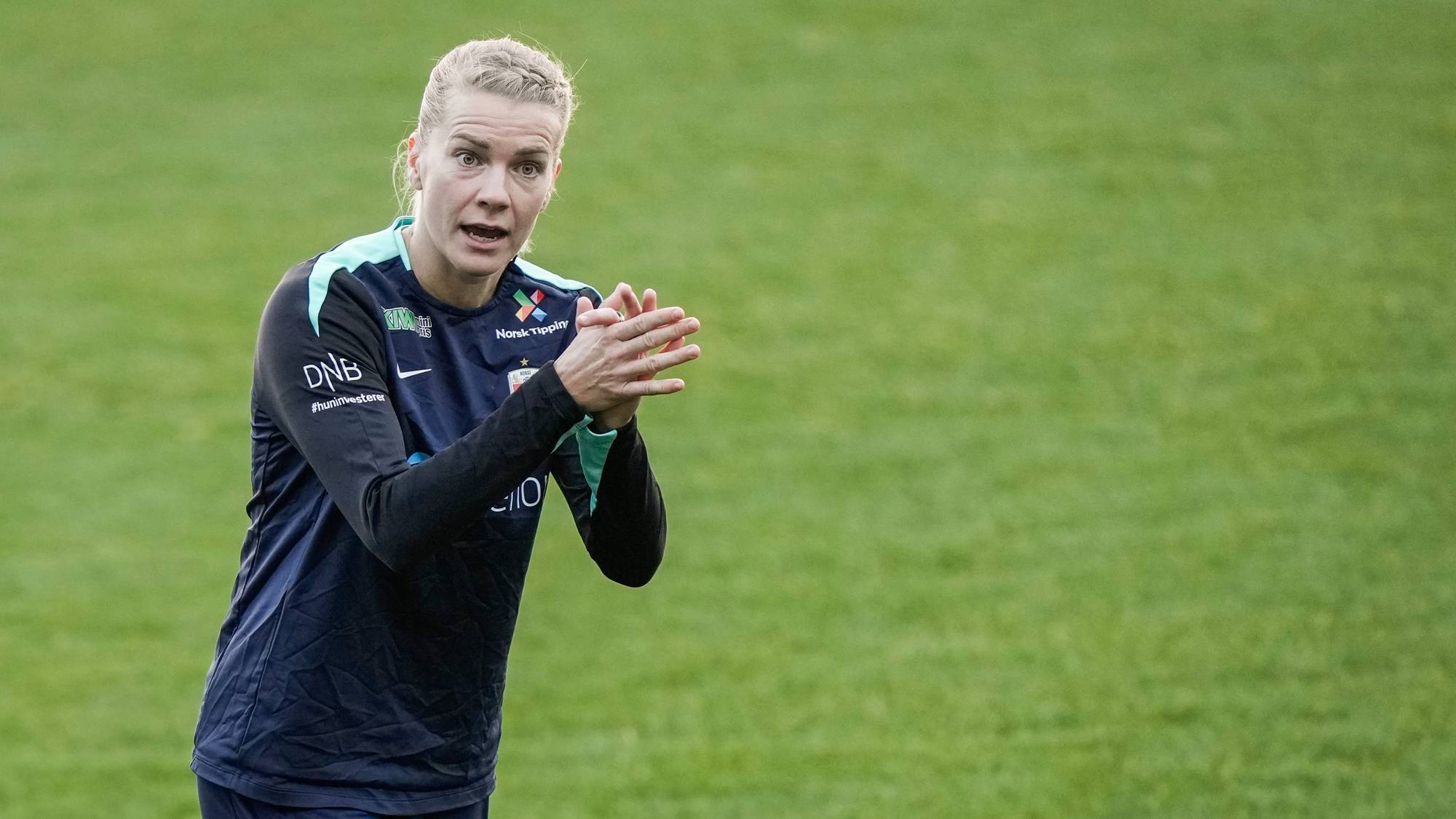 Fotballspiller i mørk drakt klapper under trening på en gressbane. (Bildebeskrivelsen er laget av en KI-tjeneste)