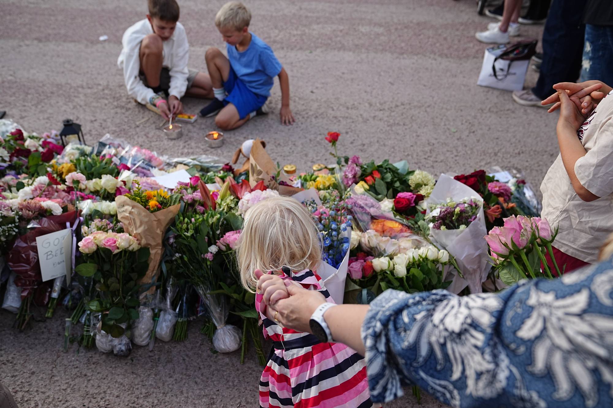 En liten jente legger ned blomster i en haug med buketter på Slottsplassen. 