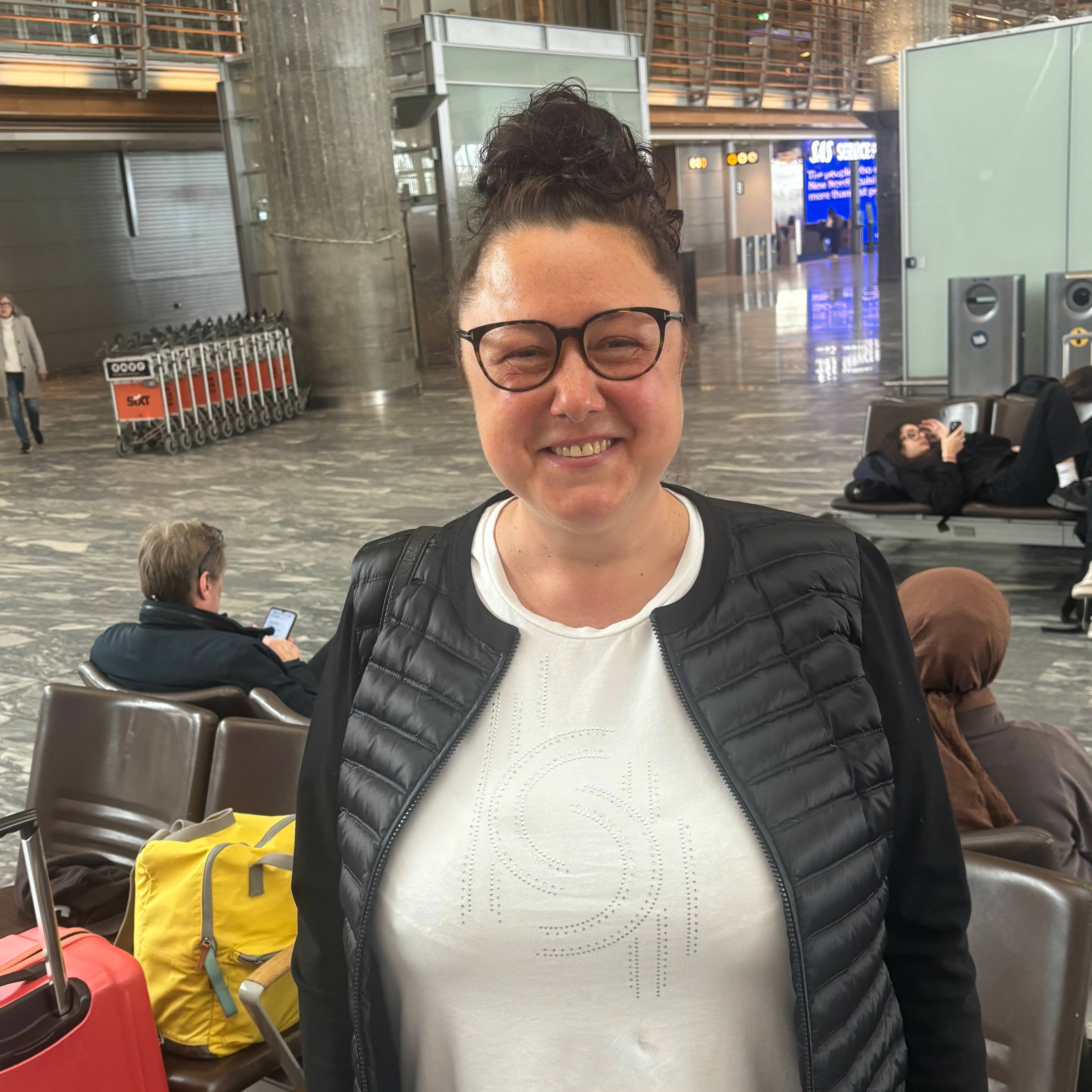 En kvinne står foran en rød koffert og en gul bag på en flyplass.