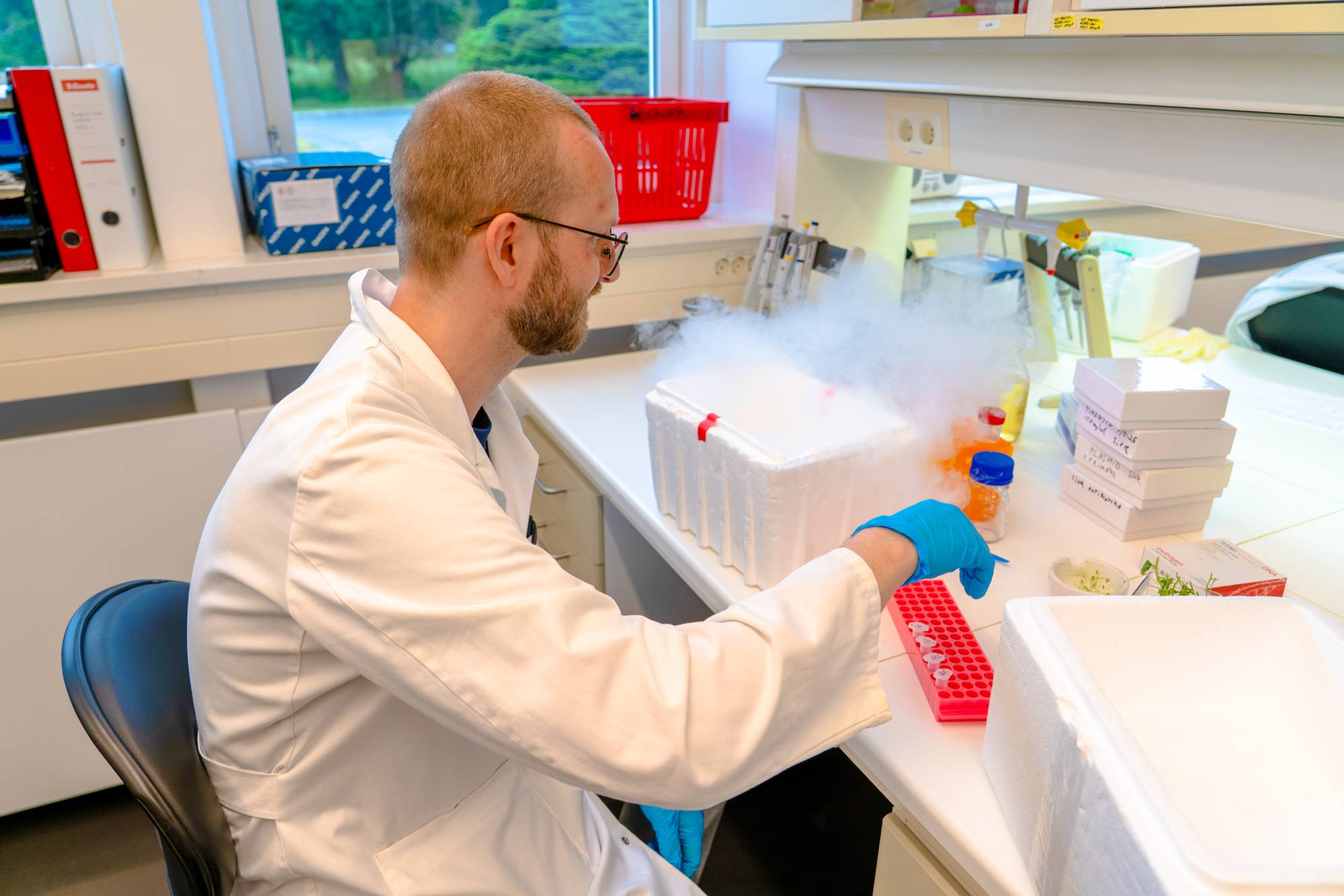 Ein person i laboratoriefrakk viser noko av forskinga han gjer på laboratoriet.