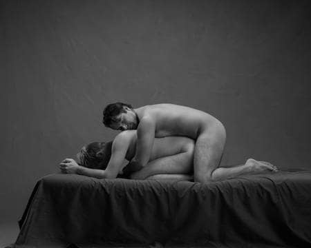 En naken mann ligger sammenkrøket på alle fire med en annen naken mann liggende over ham