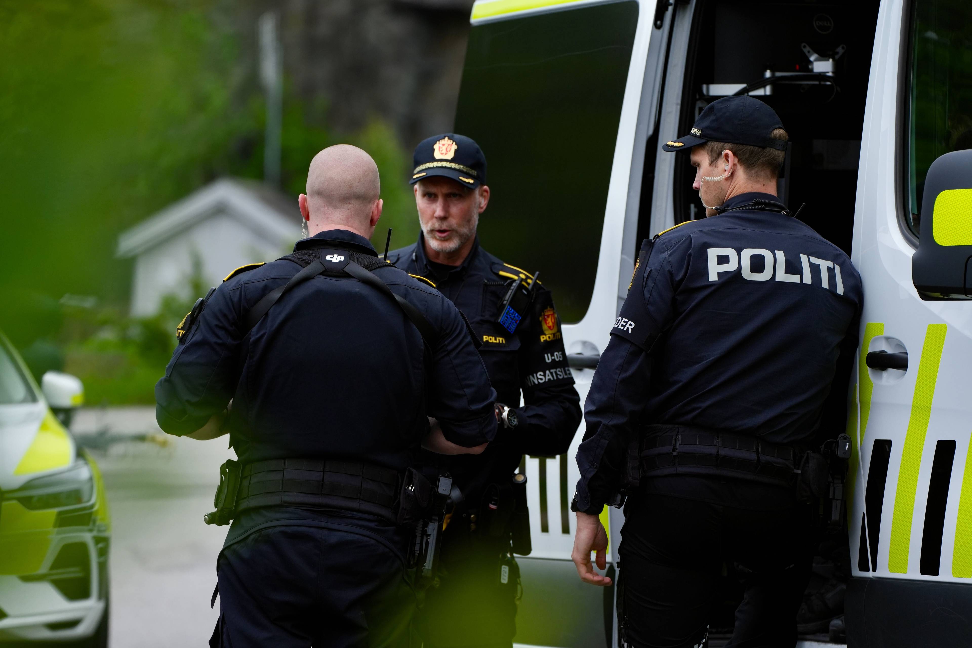 Tre politibetjenter står ved siden av en politibil. En betjent snakker med to andre mens han lener seg mot bilen. En tredje betjent står vendt vekk fra kameraet, med ryggen til. (Bildebeskrivelsen er laget av en KI-tjeneste)