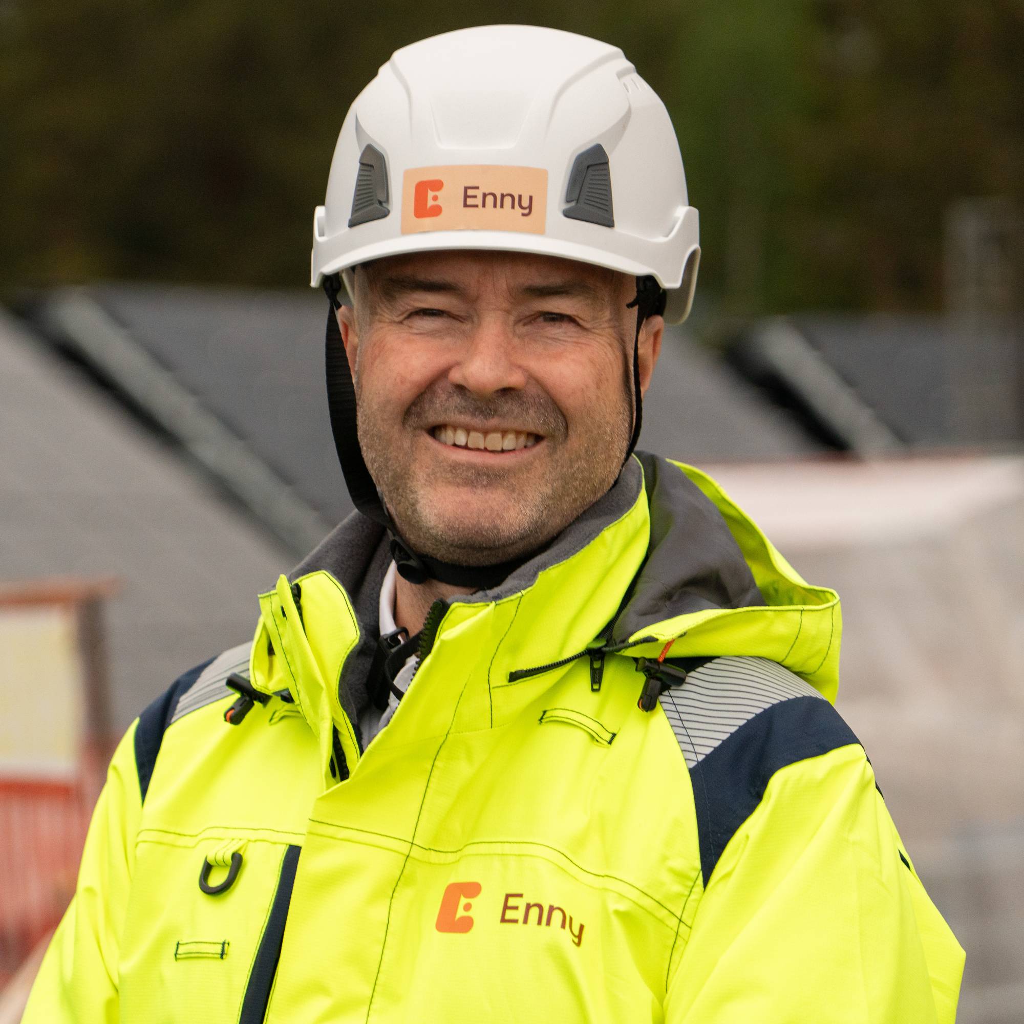Mann som smiler står ute på en byggeplass med hvit hjelm på hodet.