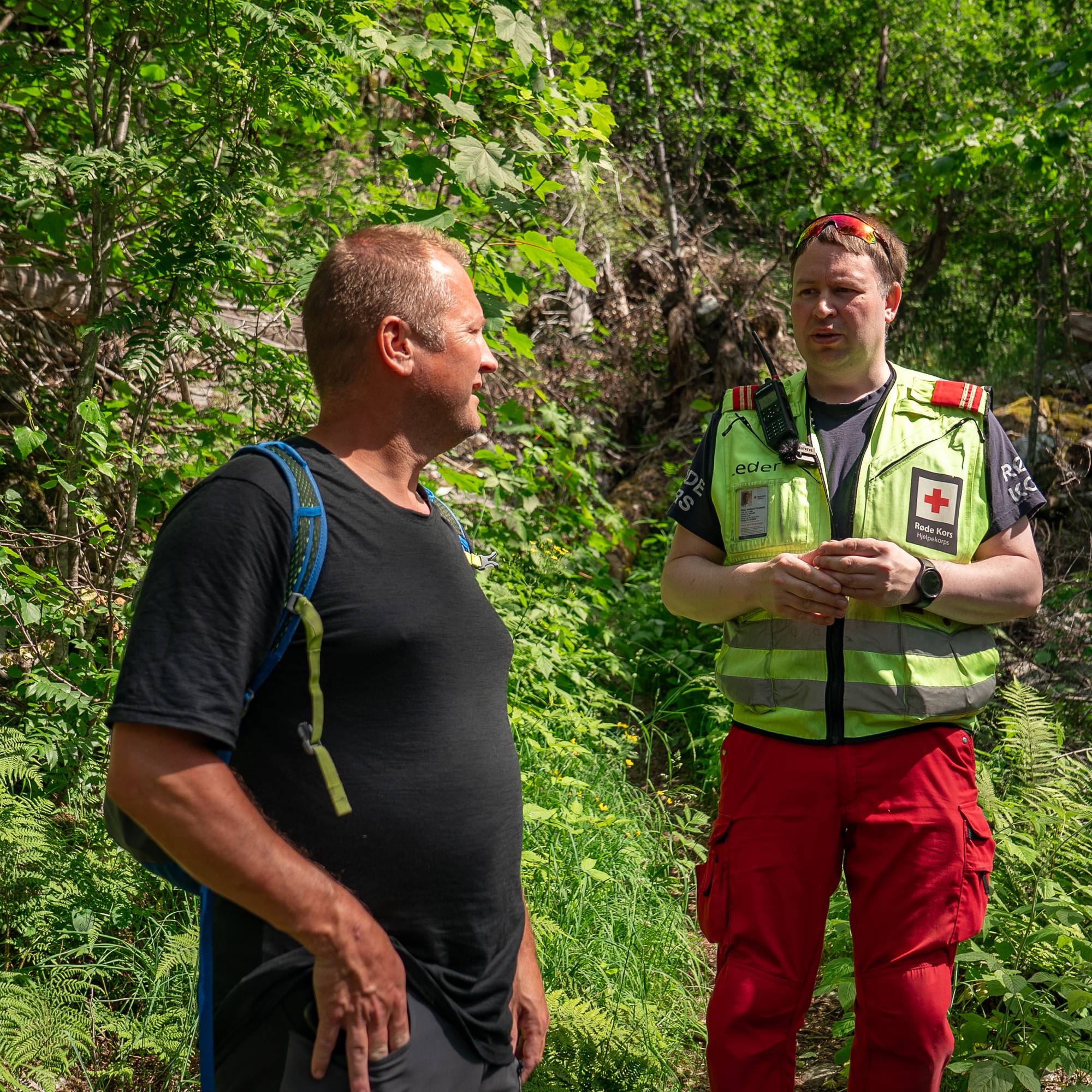 Ebn mann med sekk snakker med en mann fra Røde Kors på en tursti. 