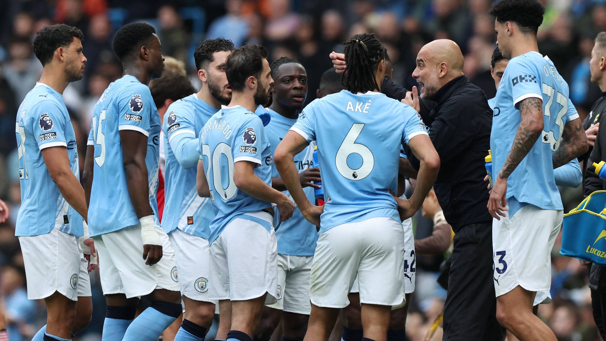 Manchester City-trener Pep Guardiola gir instruksjoner til spillere i lyseblå drakter på banen. (Bildebeskrivelsen er laget av en KI-tjeneste)