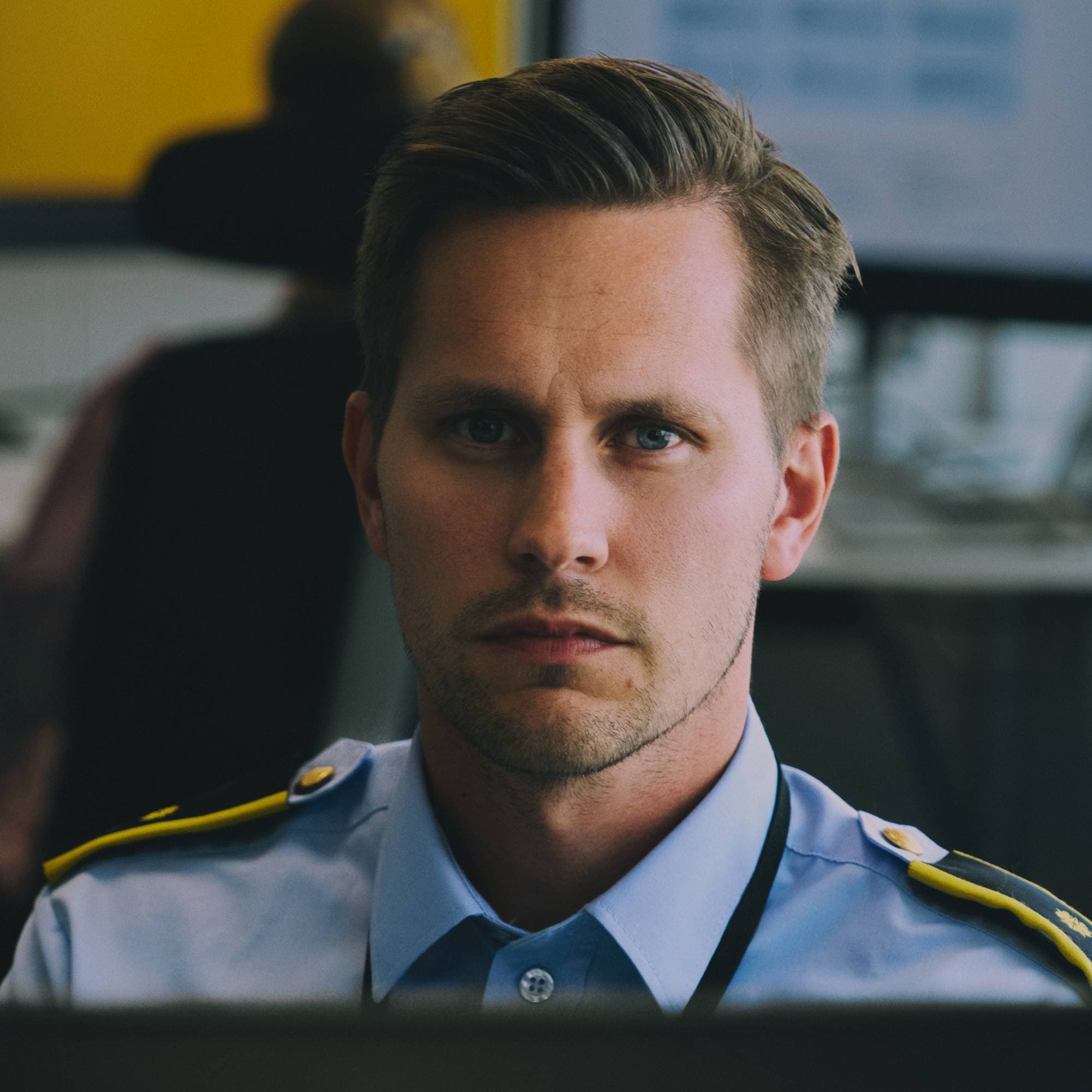 Mann i politiuniform sitter ved en datamaskin på et kontor og ser mot kameraet.