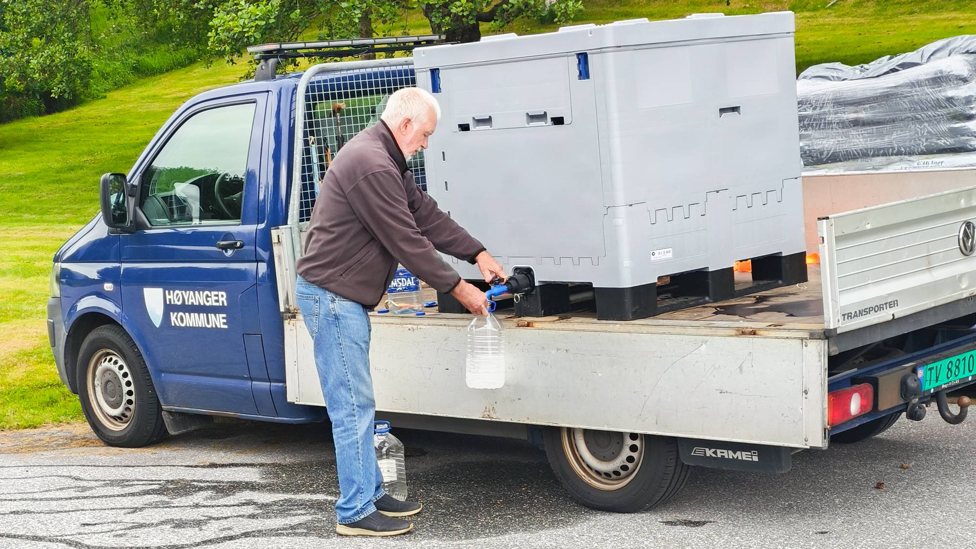 ein mann fuller vatn frå ein tank bakpå ein bil