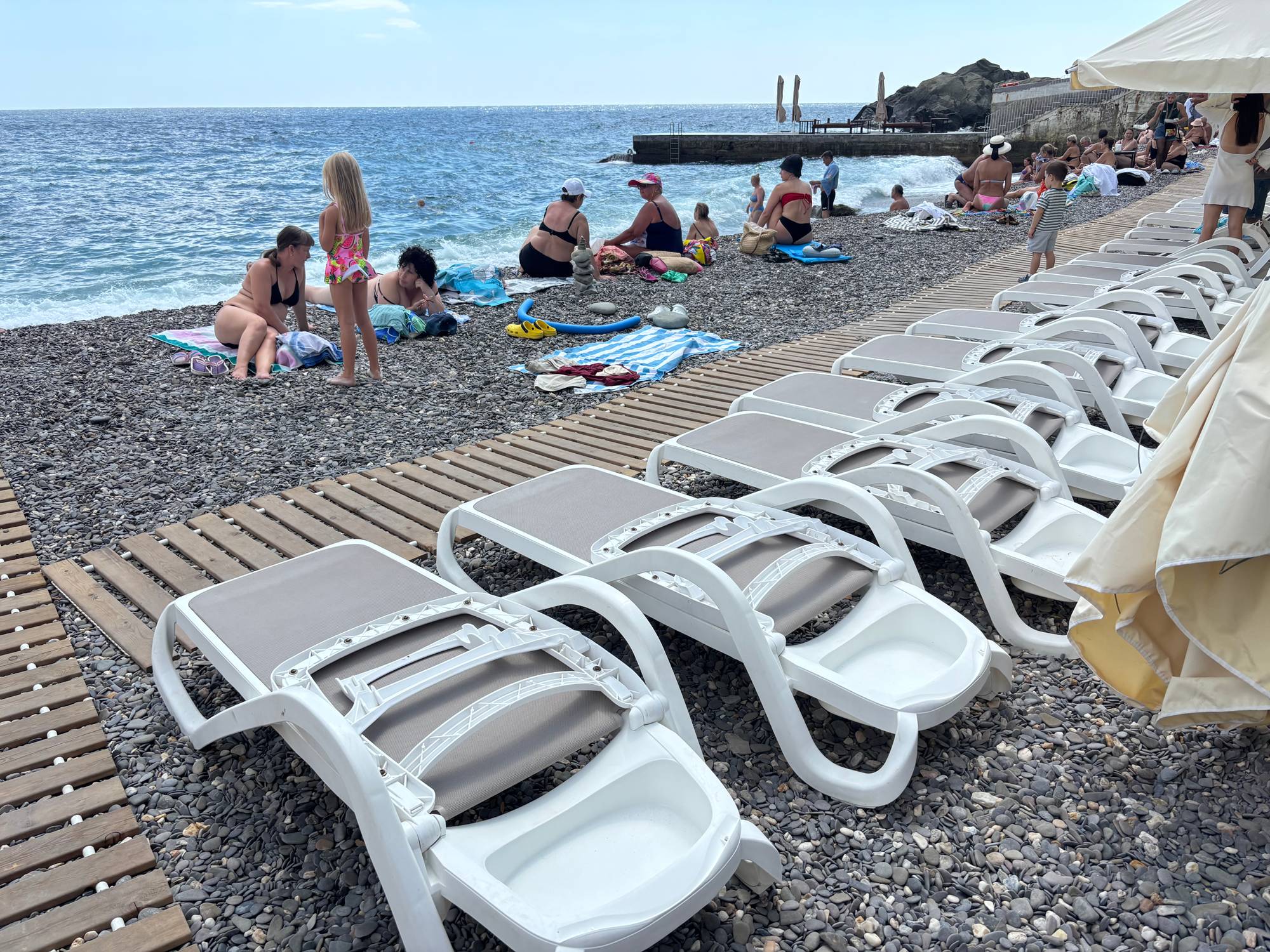 Mange tomme solstoler på en steinstrand.