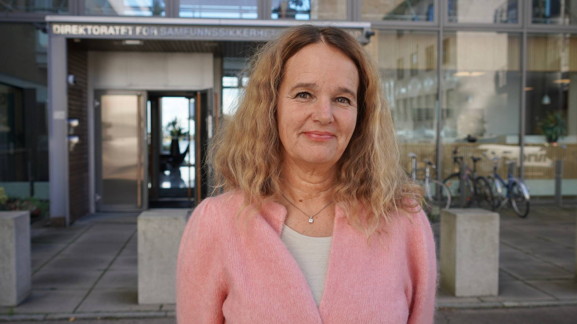 Kvinne med blondt hår står foran inngangen til Direktoratet for samfunnssikkerhet og beredskap. (Bildebeskrivelsen er laget av en KI-tjeneste)