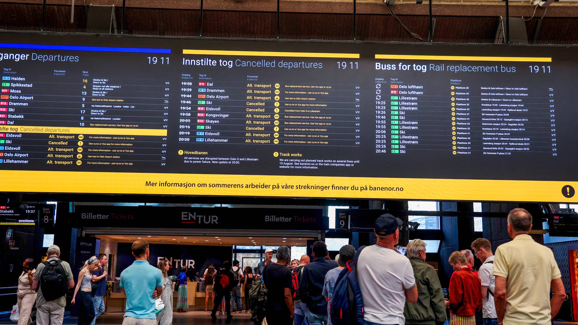 Reisende ser på en informasjonstavle med oversikt over innstilte tog og buss for tog på en stasjon. (Bildebeskrivelsen er laget av en KI-tjeneste)