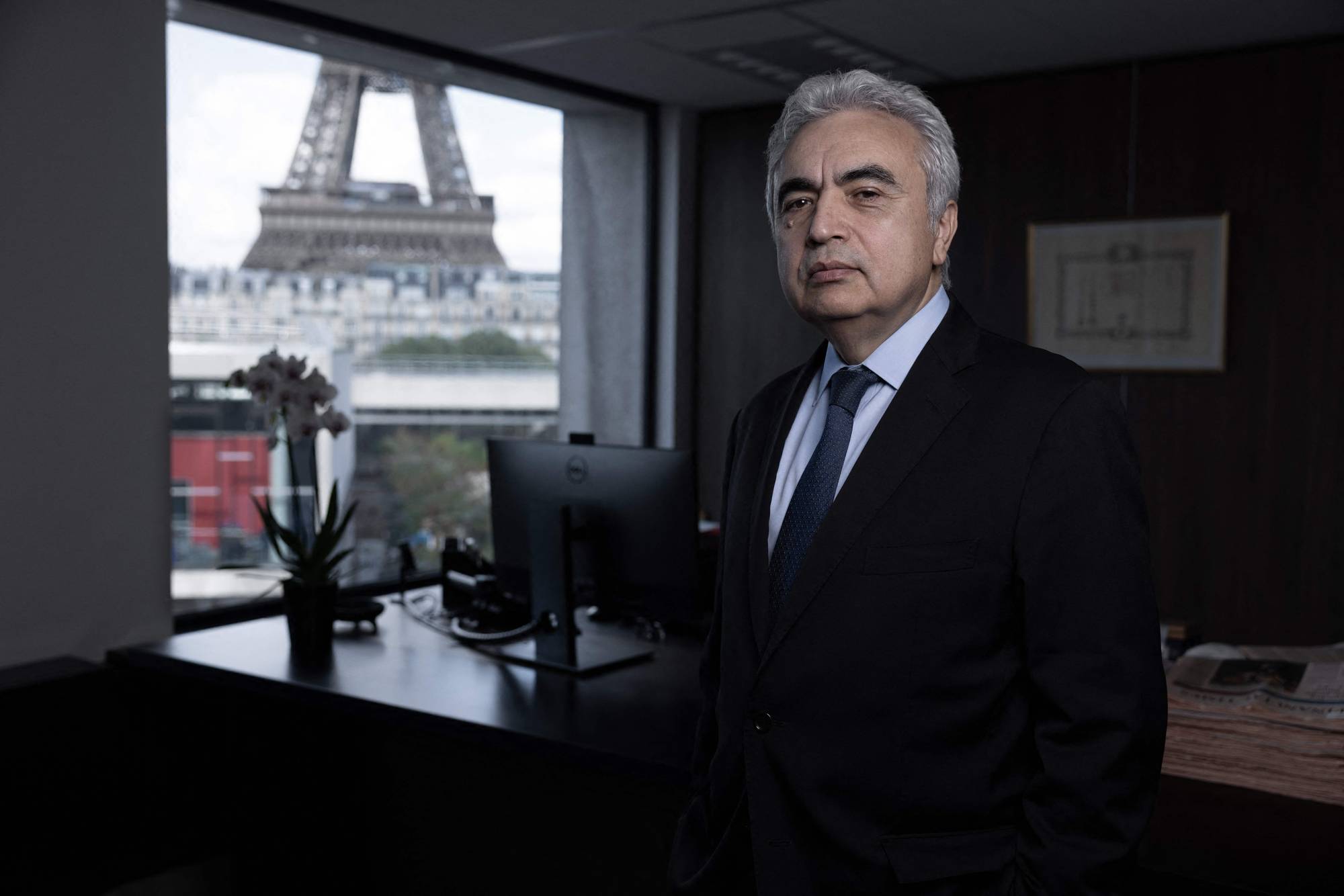 Fatih Birol i dress på et kontor med Eiffeltårnet synlig gjennom vinduet. (Bildebeskrivelsen er laget av en KI-tjeneste)