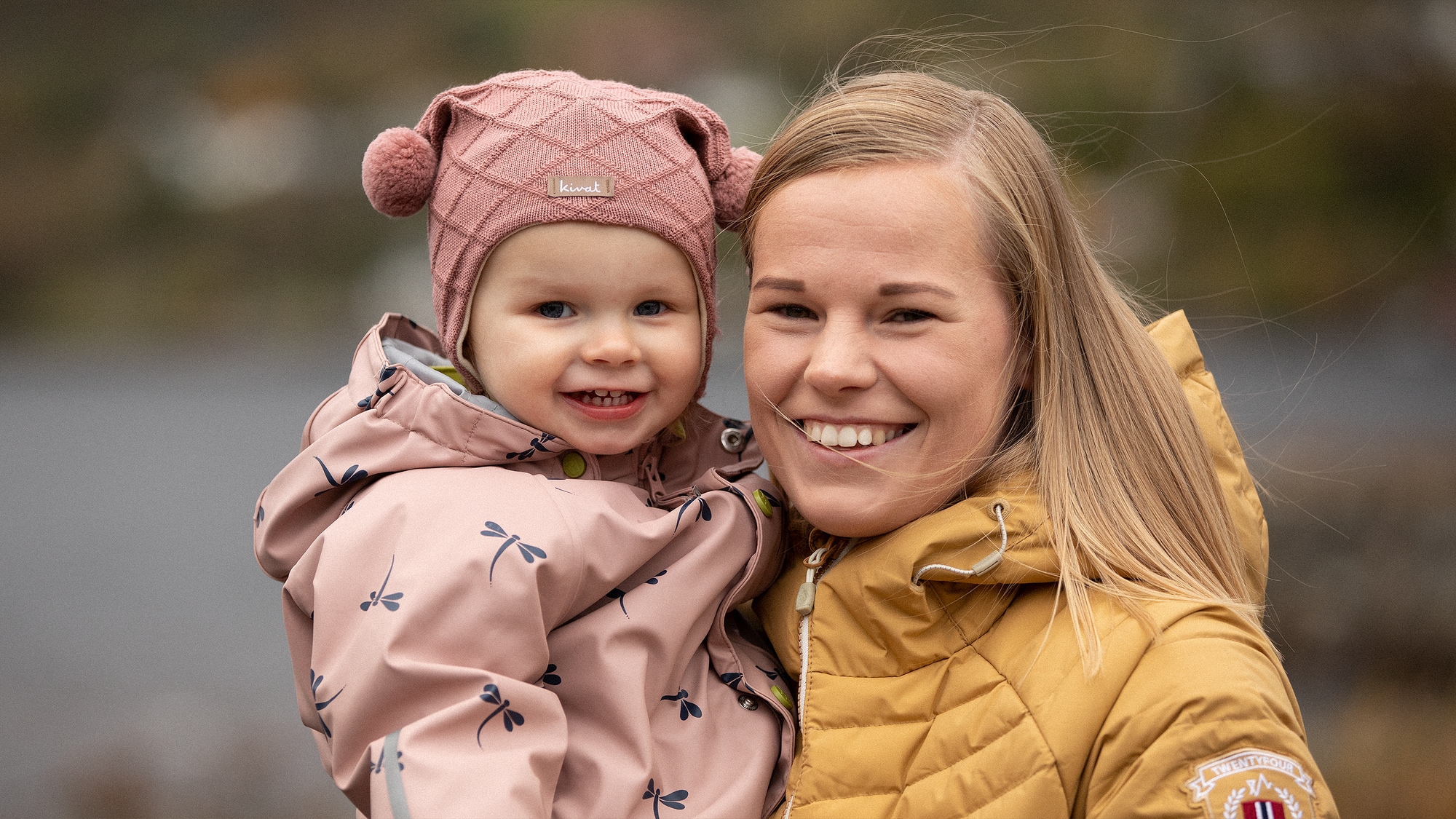 Portrett av Daniëlle og datteren på 1,5 år. Daniëlle har på seg en gul jakke og smiler bredt med tennenene. Datteren er ikledd en rosa buksedress og har på seg en rosa lue. 