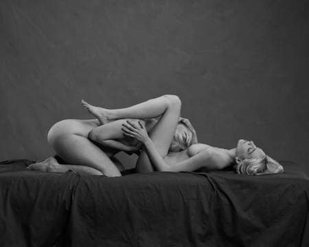 En blond kvinne ligger på en svart madrass og sprer beina. En annen blond kvinne ligger med ansiktet mellom beina hennes og simulerer oralsex. Begge er nakne, men kjønnsorganene er ikke synlige.
