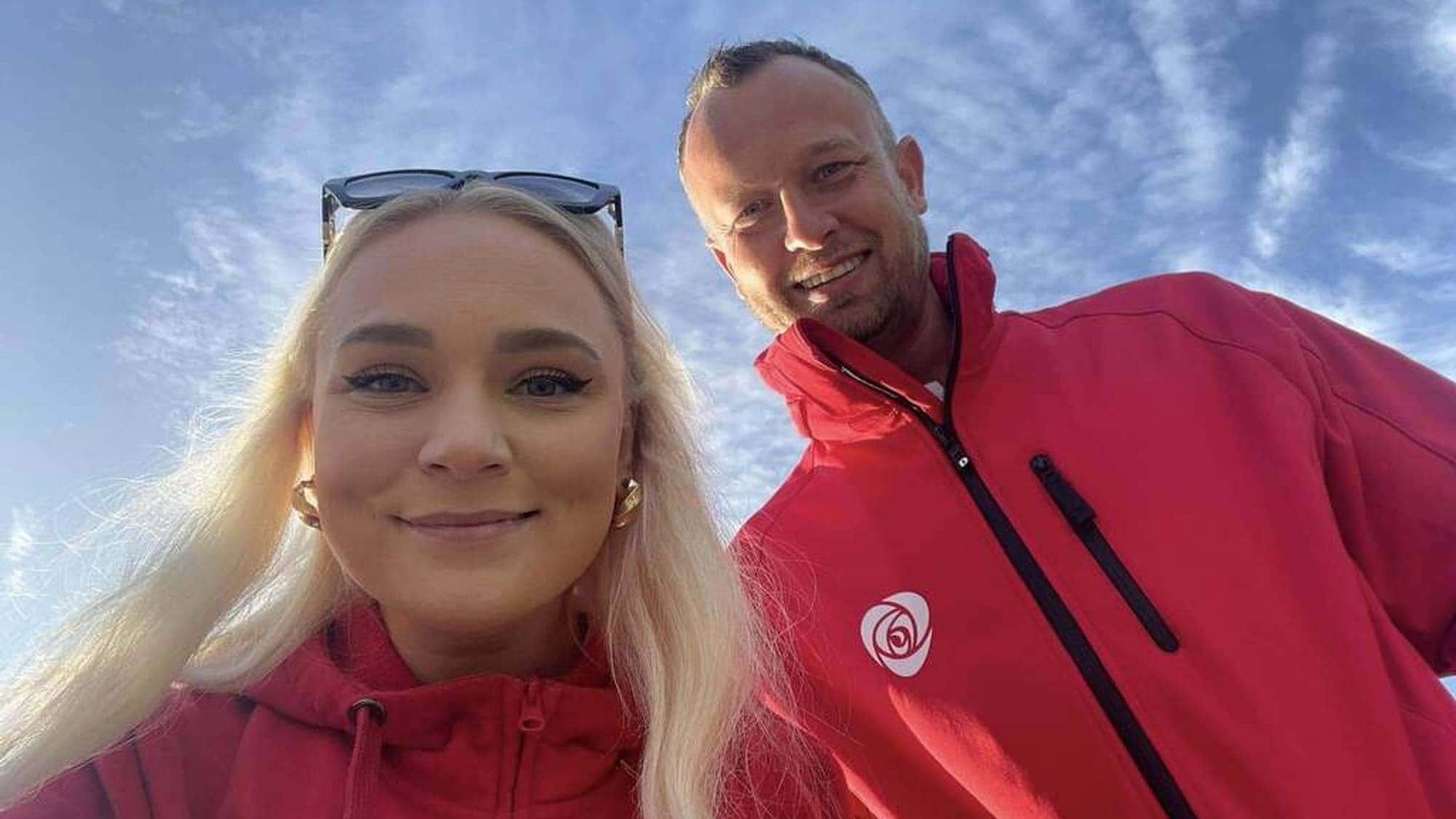 En kvinne med langt lyst hår og en mann bøyer seg over kamera og smiler. 