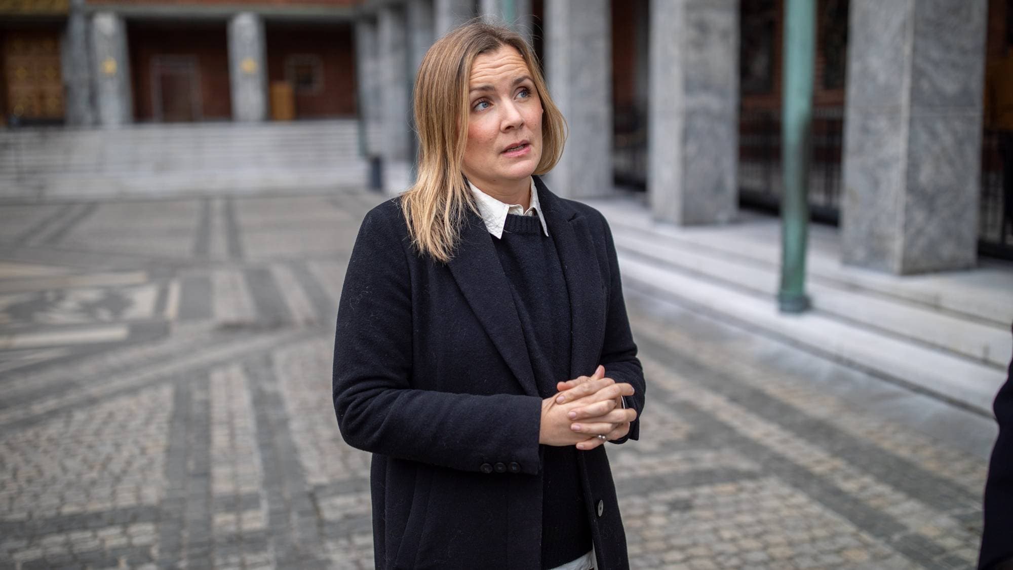 Marit Vea, en kvinne i mørk frakk over en mørk genser står i borggården til Oslo rådhus