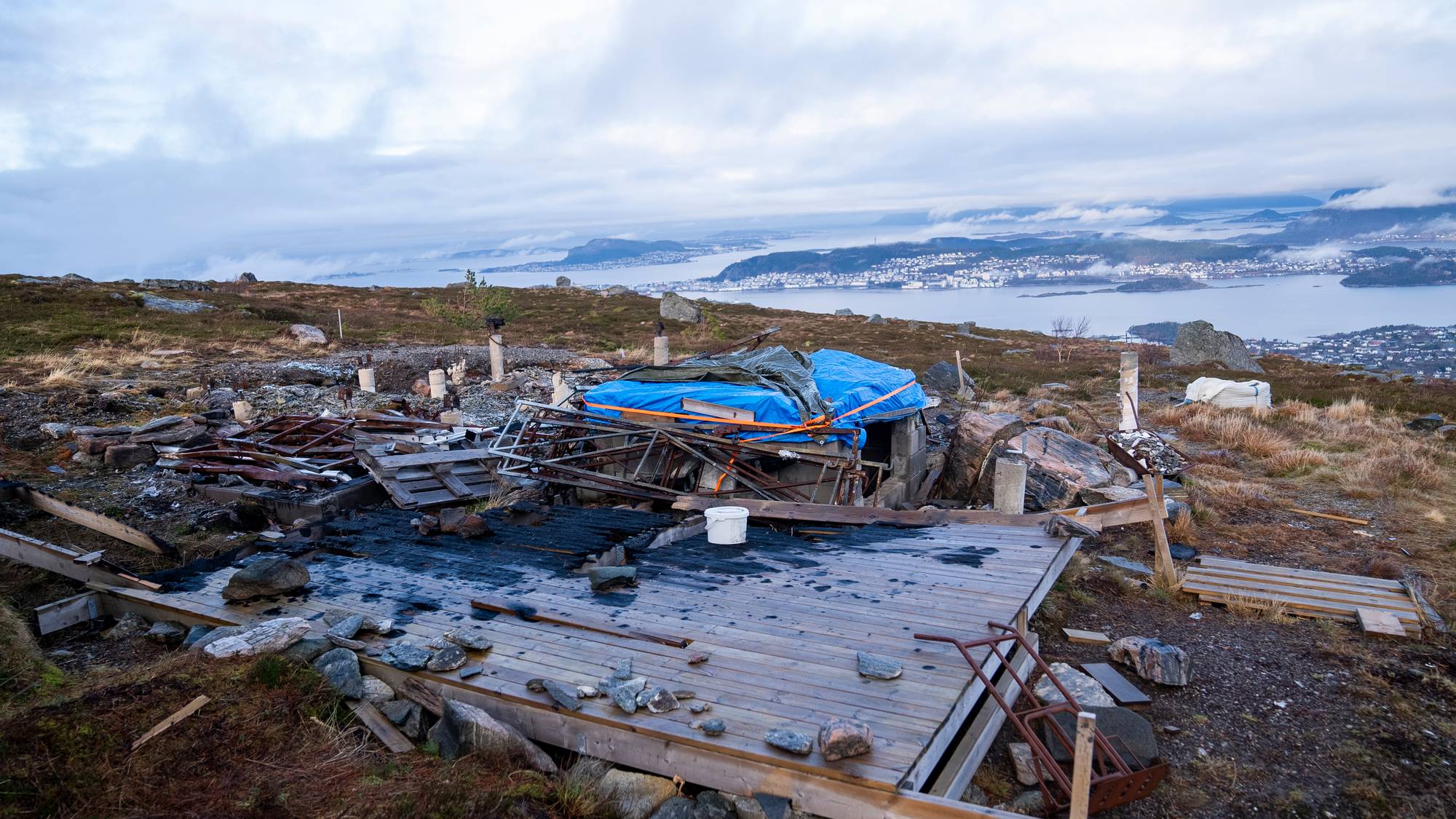 Ei gamal branntomt på Sulafjellet, ein ser rester etter ei hytte og Ålesund i bakgrunnen.