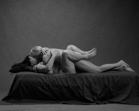 En naken dame ligger på ryggen og kysser en naken mann som ligger oppå henne. Bena hennes er bøyd over ryggen hans