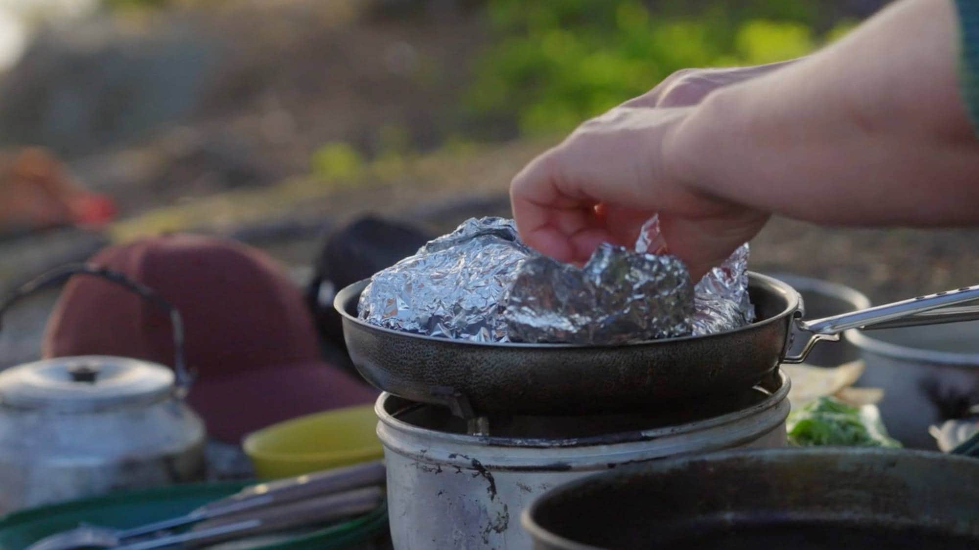 Mat i folie varmes opp på primus. To hender tar i pakken med aluminiumsfolie.