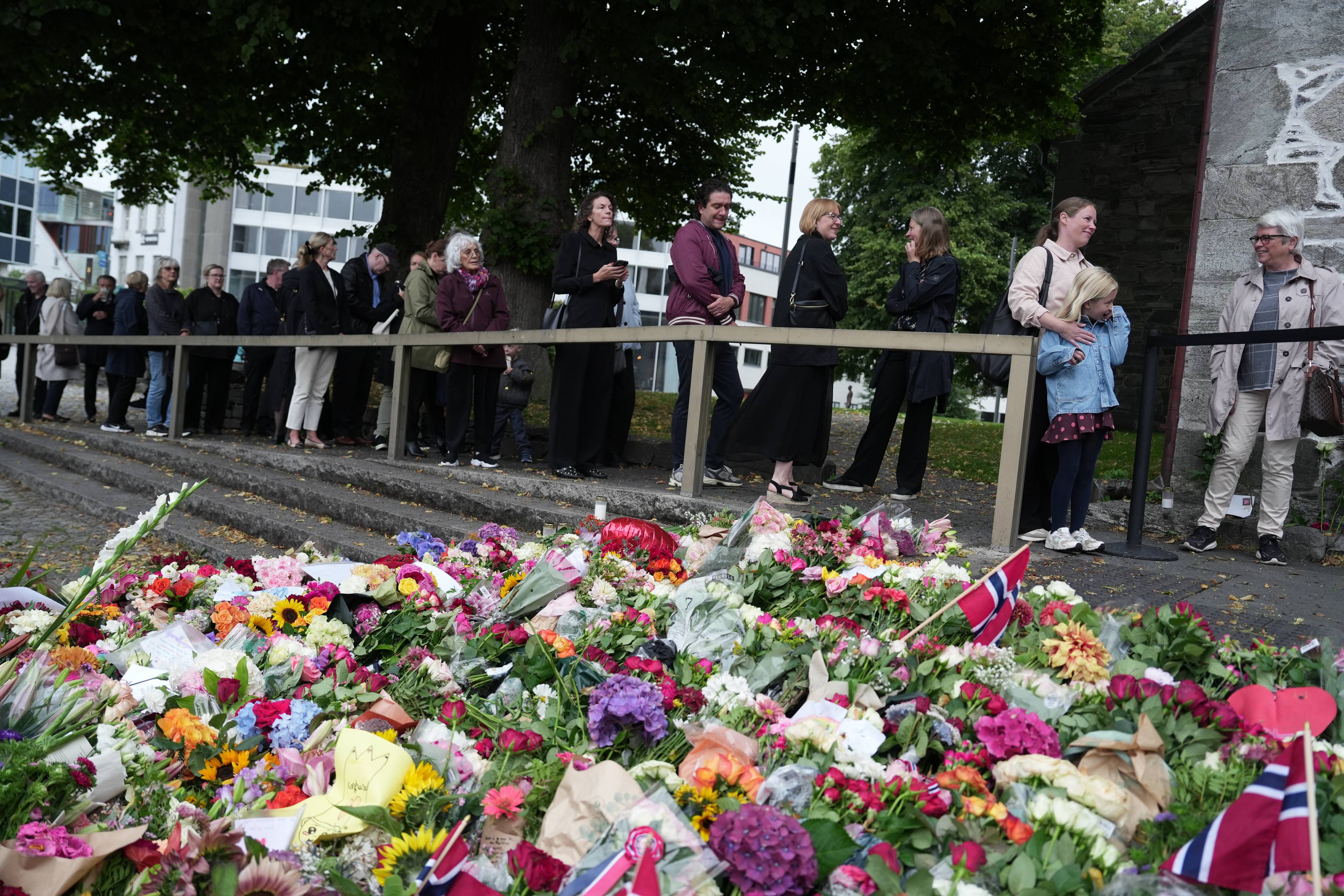 Folk står i kø for å legge ned blomster ved et minnested etter kong Harald V sin død.