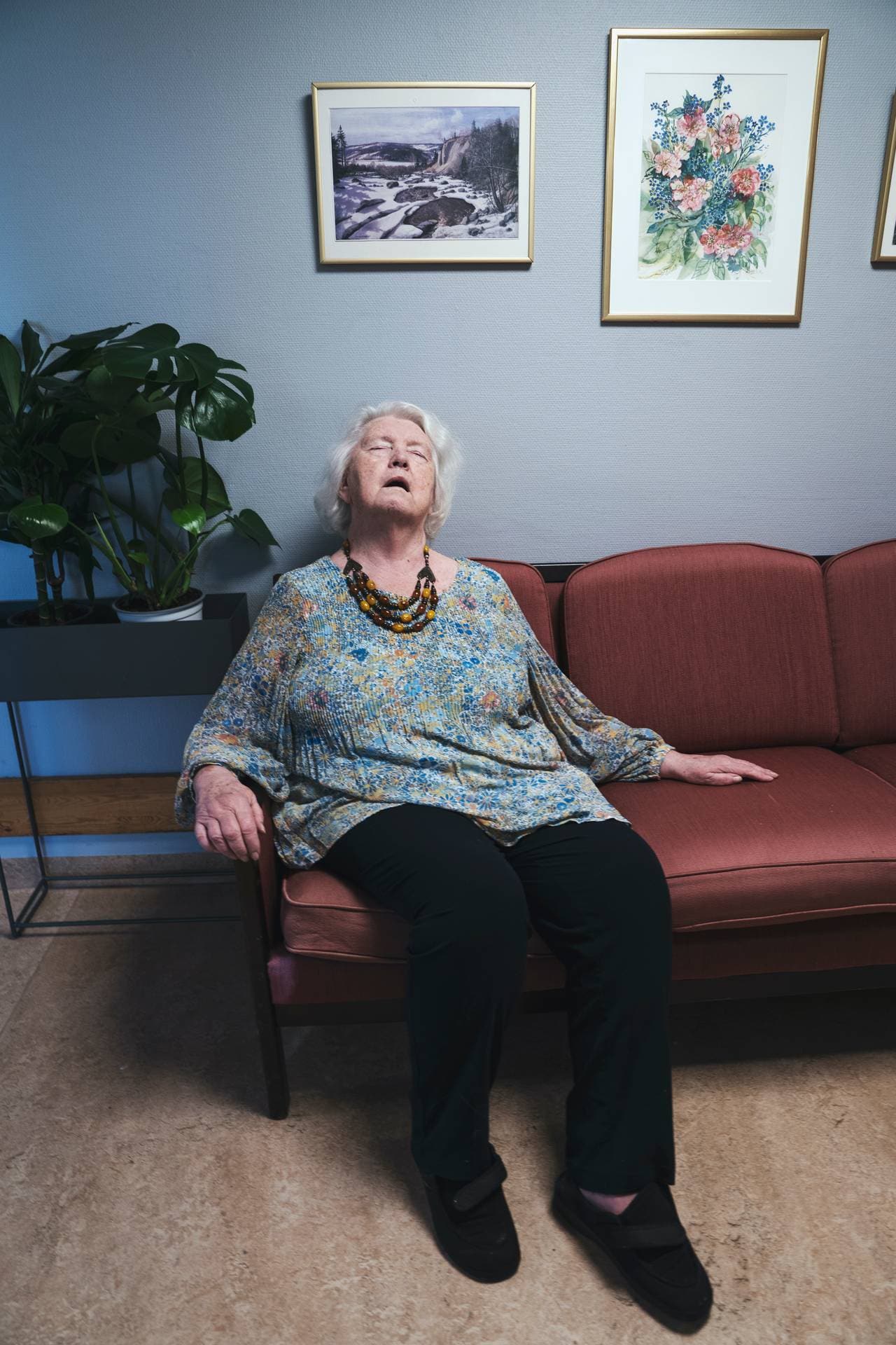 Anne Marie sitter i en eldre sofa i gangen og lukker øynene med åpen munn.