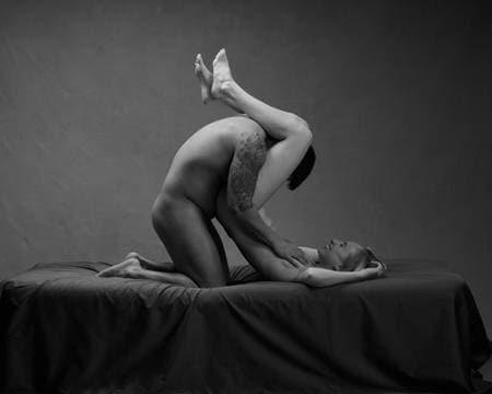 En naken kvinne, blond og slank, ligger med bekkenet og beina i være. En naken mann med tatoveringer på armen, kneler og lener seg mellom beina hennes og simulerer oral sex.