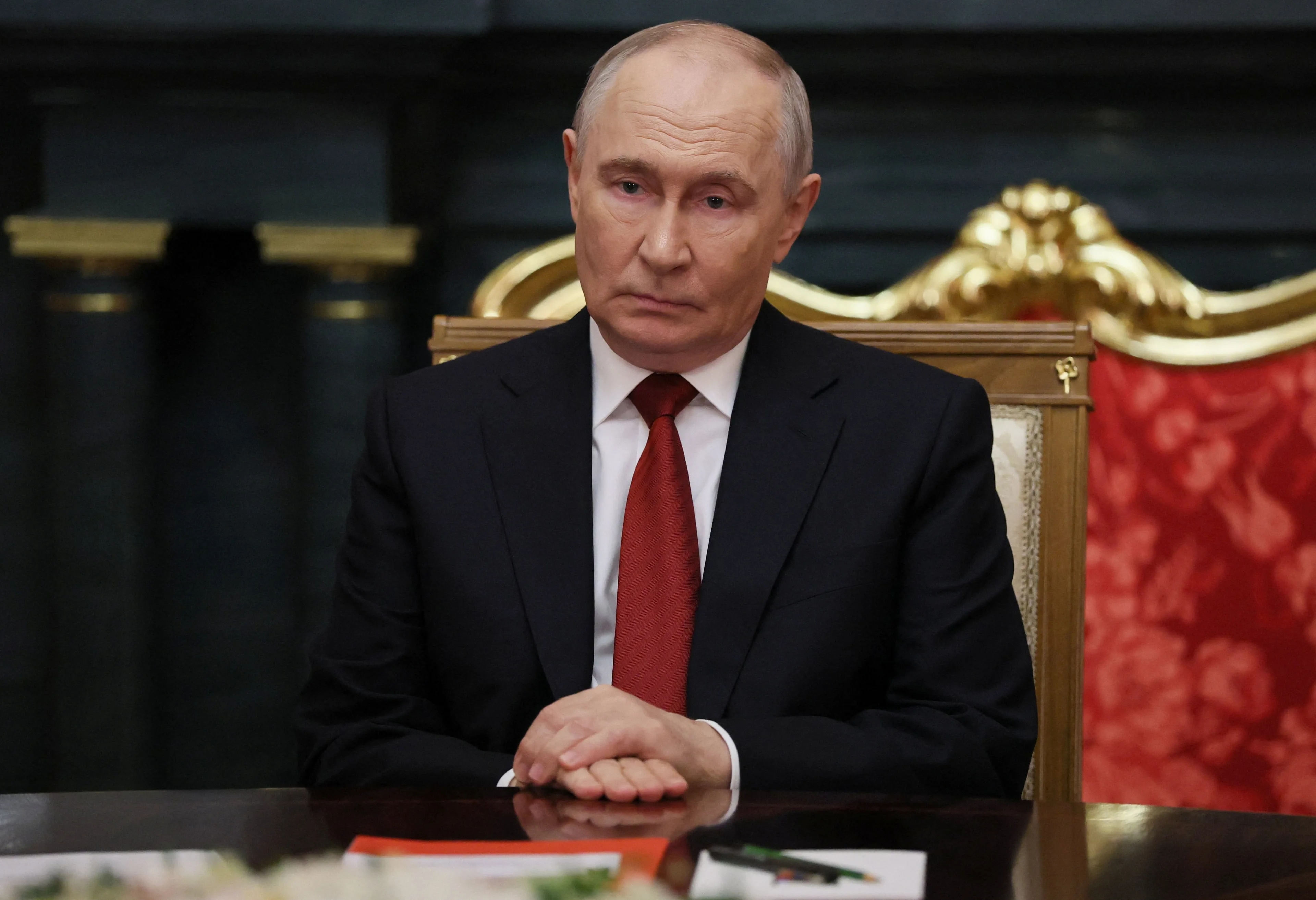 Vladimir Putin sitter ved et bord i en stol med rødt trekk. (Bildebeskrivelsen er laget av en KI-tjeneste)