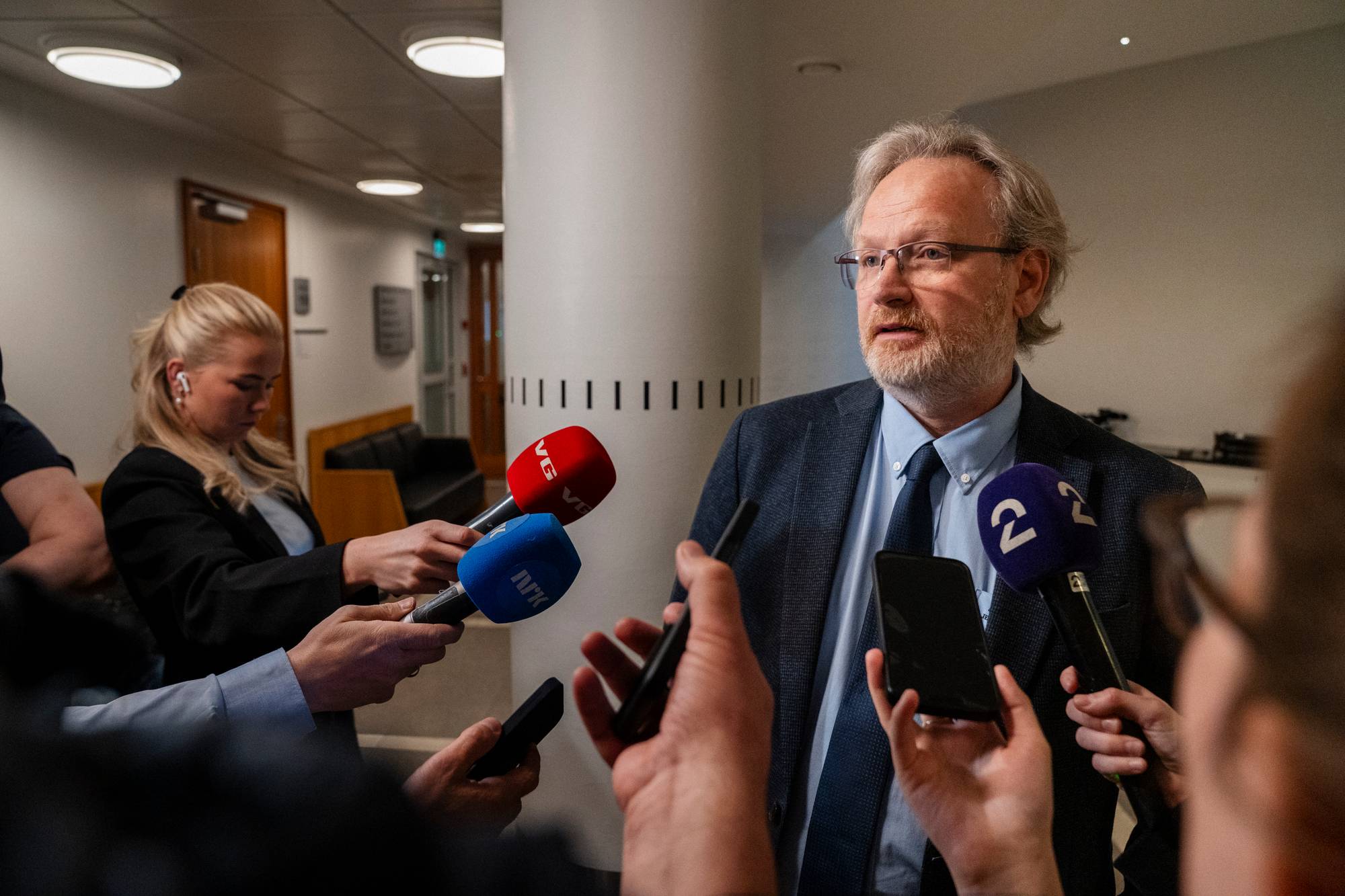 En mann i dress blir intervjuet av mange pressefolk inne i Oslo tingrett.