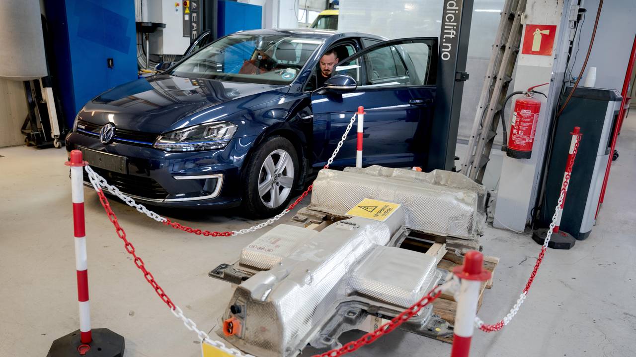 Blå e-golf i bakgrunnen med det gamle batteriet i forgrunnen, inngjerdet med gule varsler om høyspenning