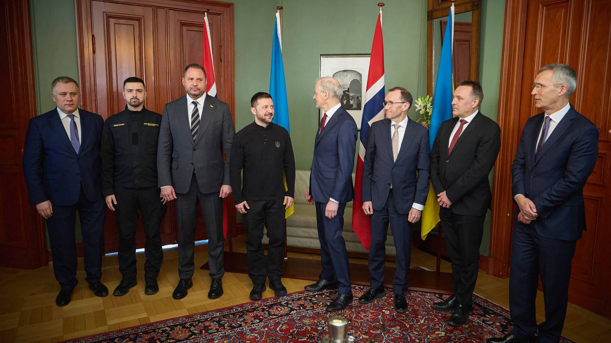 Åtte menn i dress står framfor norske og ukrainske flagg. 