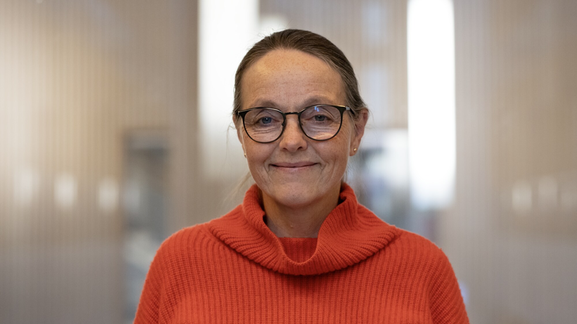 Kvinne med mørkt hår og rød genser kikker i kamera