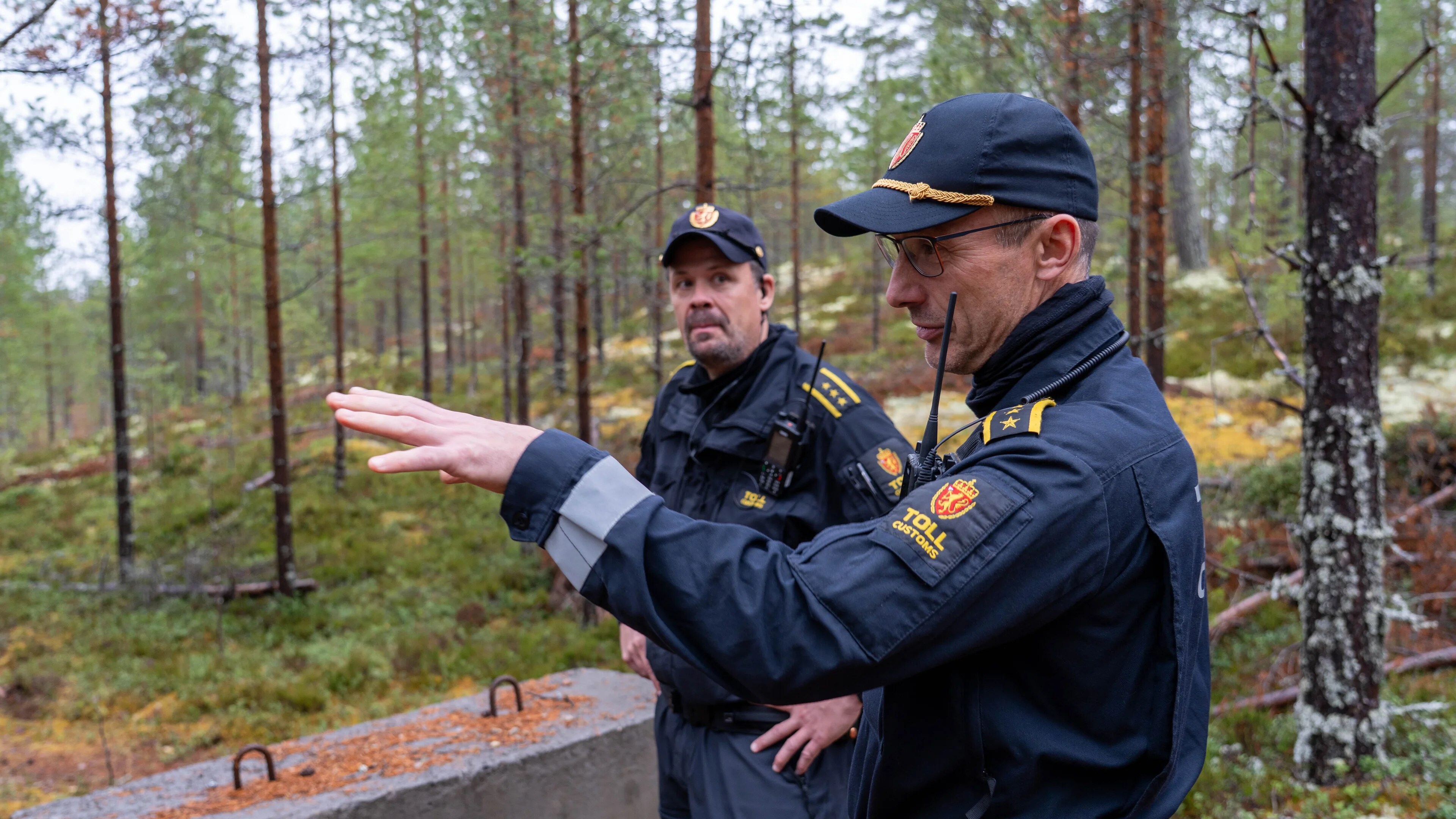 Toller står i skogen i Trysil og peker, men kollega i bakgrunnen.