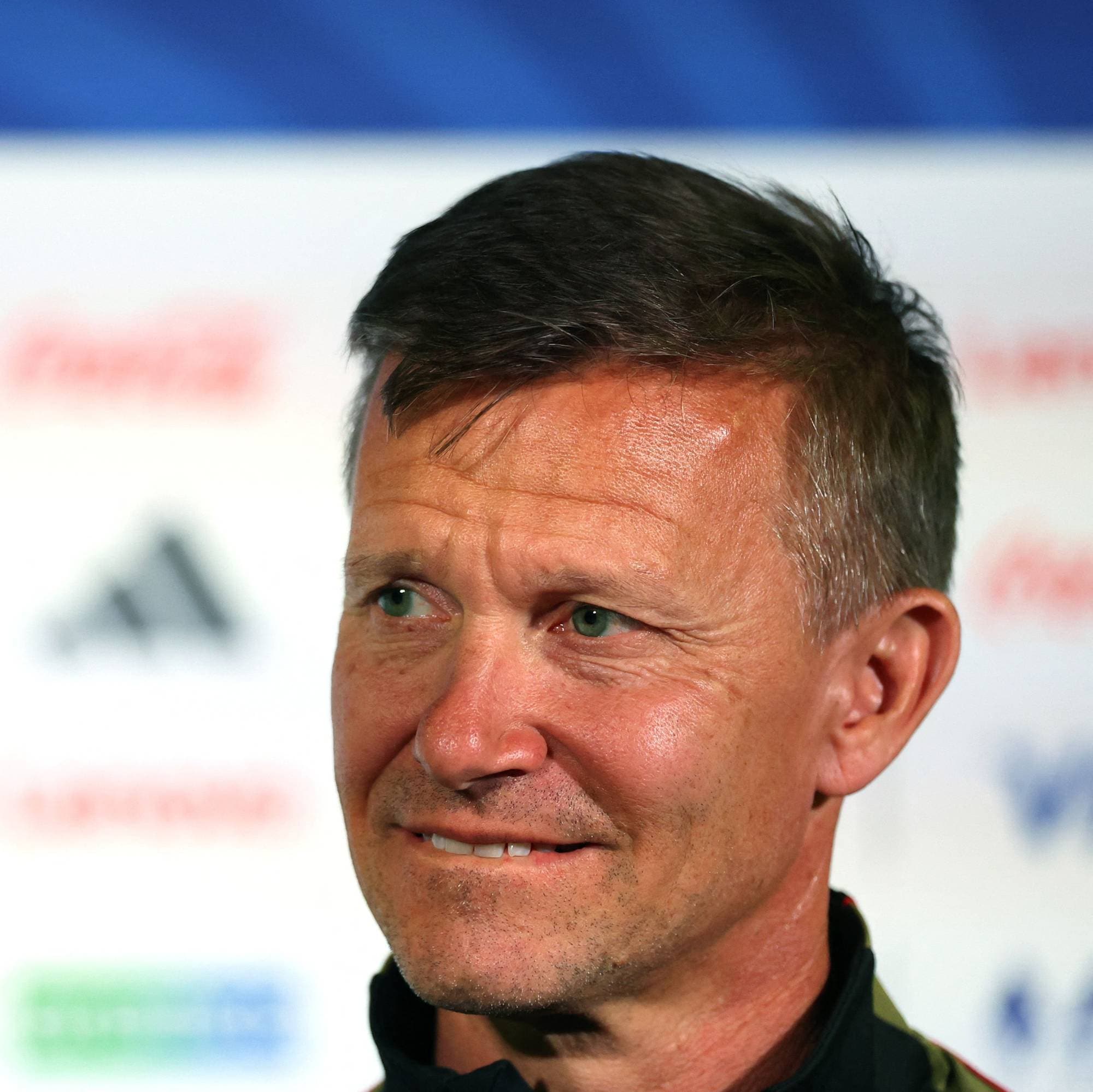 Fotballtrener Ståle Solbakken foran en bakgrunn med sponsorlogoer. (Bildebeskrivelsen er laget av en KI-tjeneste)