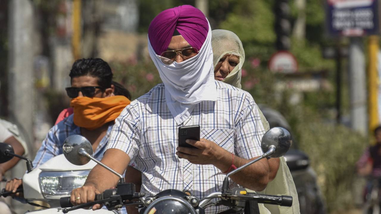Commuters cover their face with cloth to shelter from the heat as they make their way along a road in a summer afternoon in Amritsar on April 26, 2022. (Photo by NARINDER NANU / AFP)