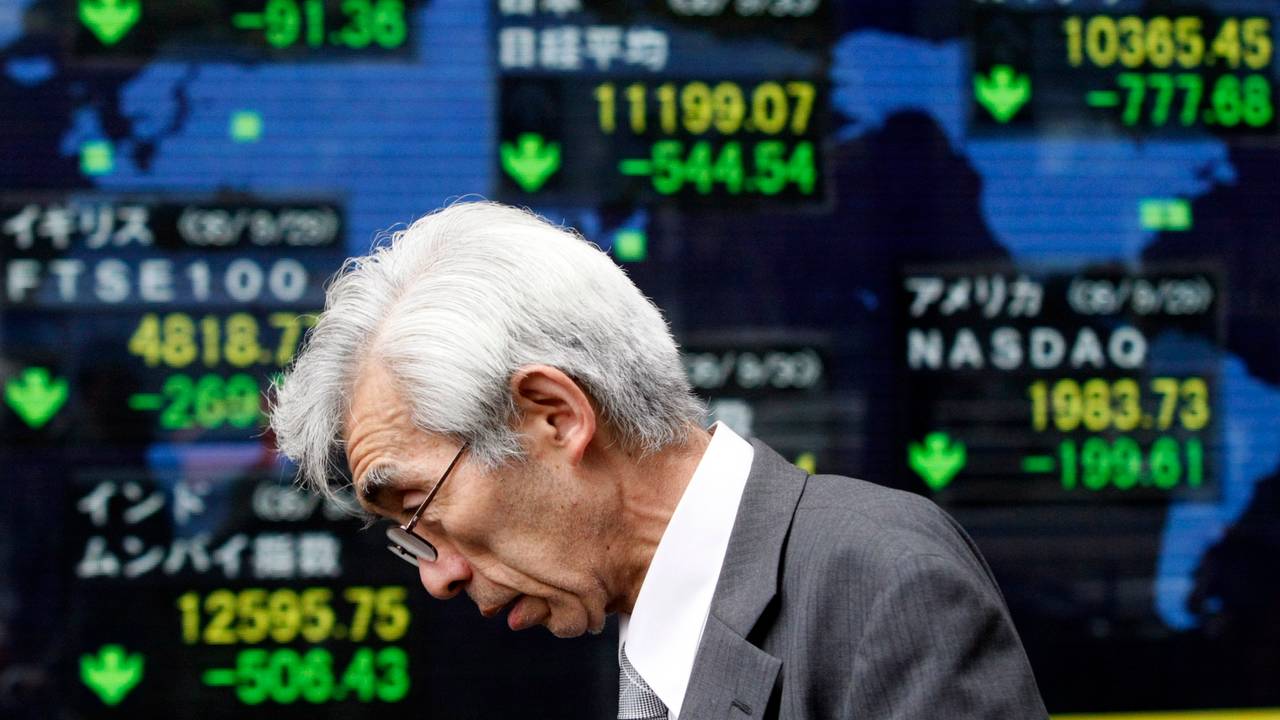 A man walks past an electronic board displaying movements in major indices in Tokyo