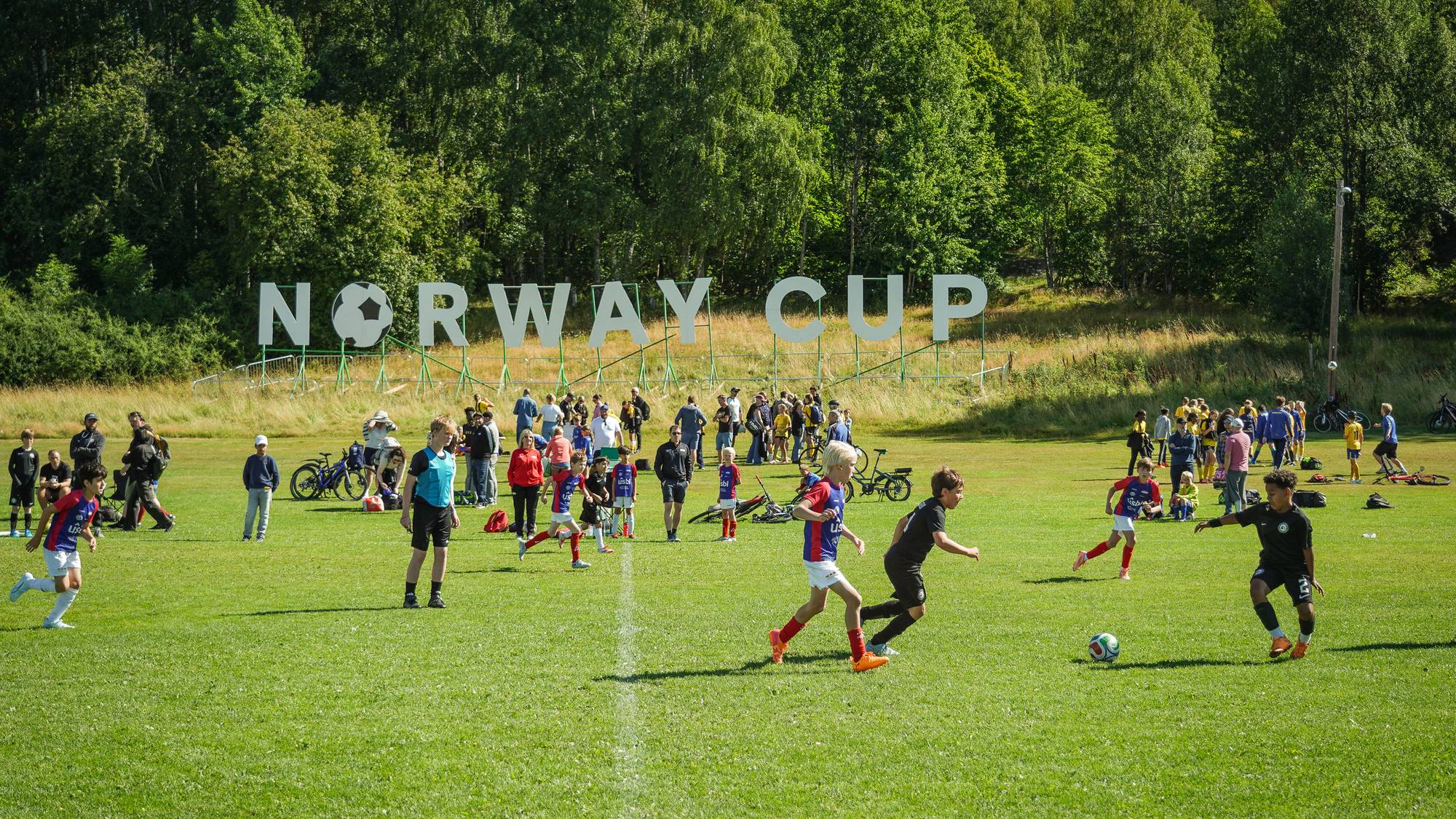 Barn som spiller fotball med et Norway Cup-skilt i bakgrunnen. 