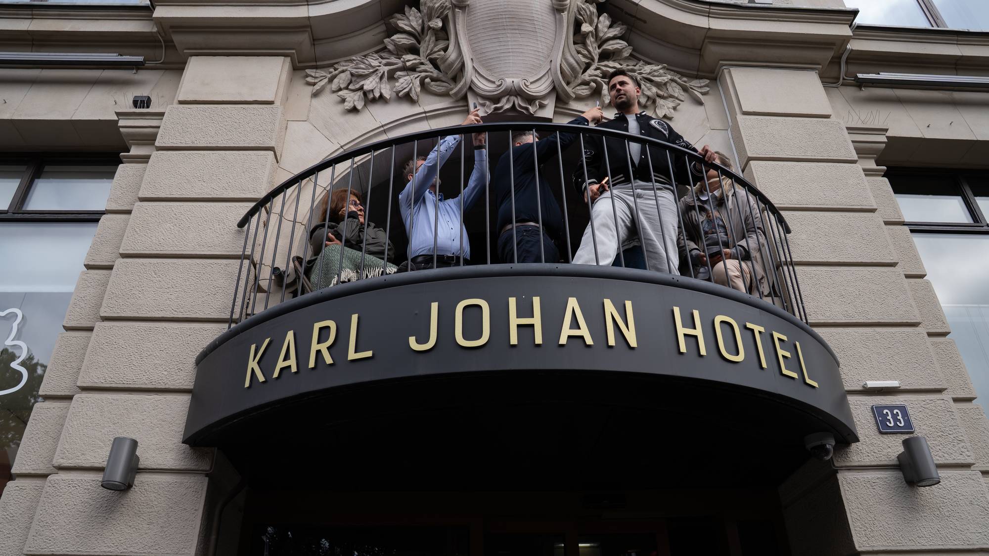 Balkongen på Karl Johan Hotel. Flere mennesker står ute på balkongen og ser utover. 