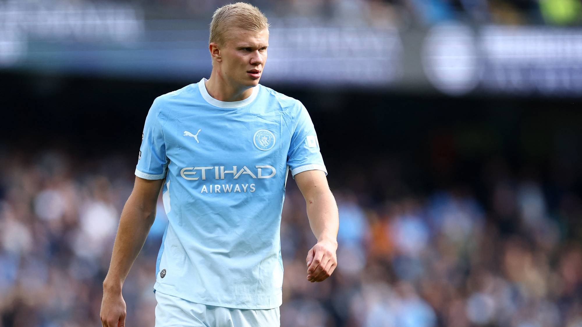 Erling Braut Haaland i Manchester City-drakt på en fotballbane med publikum i bakgrunnen. (Bildebeskrivelsen er laget av en KI-tjeneste)