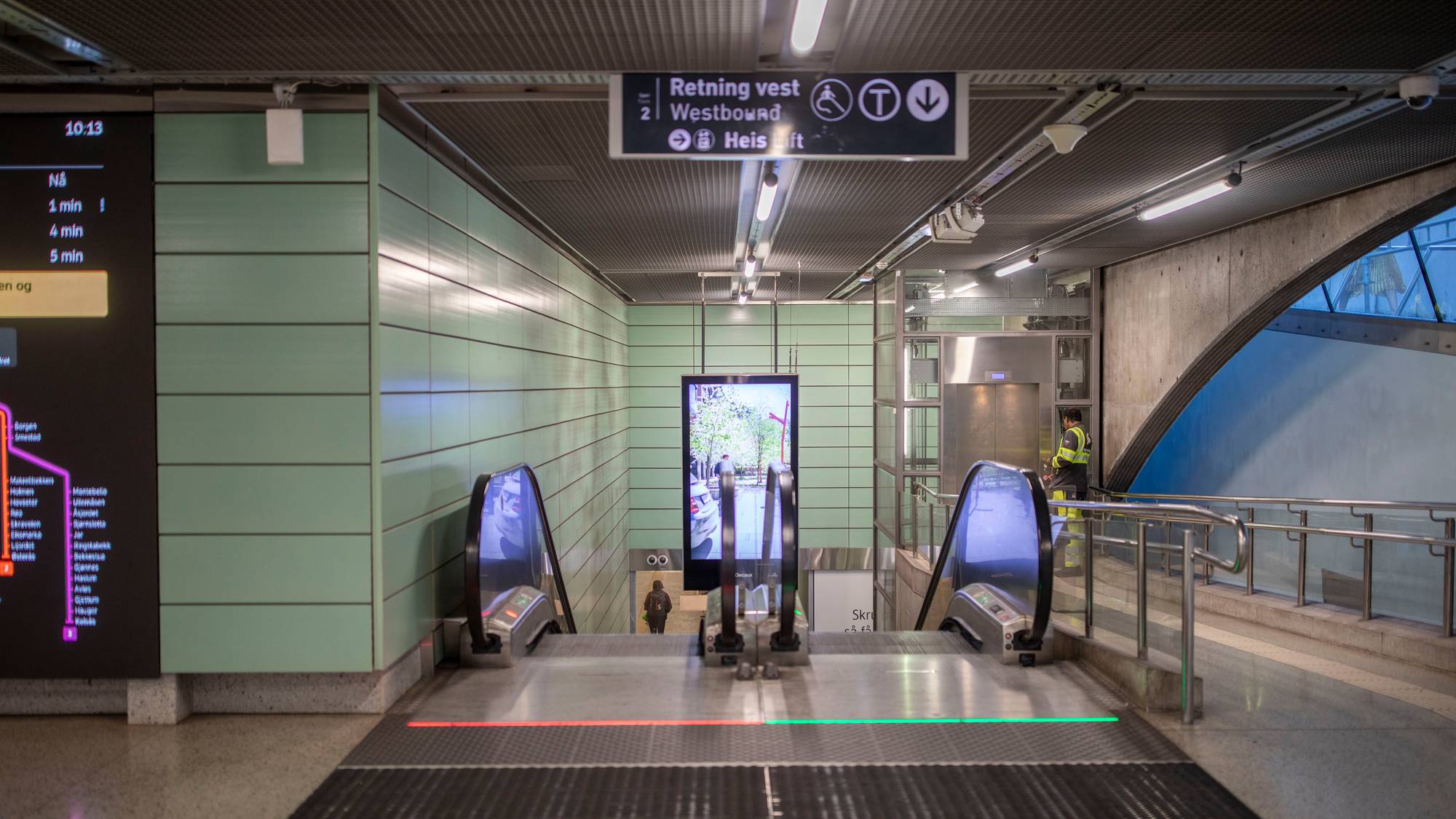 Rulletrapper og heis på en T-banestasjon. En person går ned mot perrongen. (Bildebeskrivelsen er laget av en KI-tjeneste)