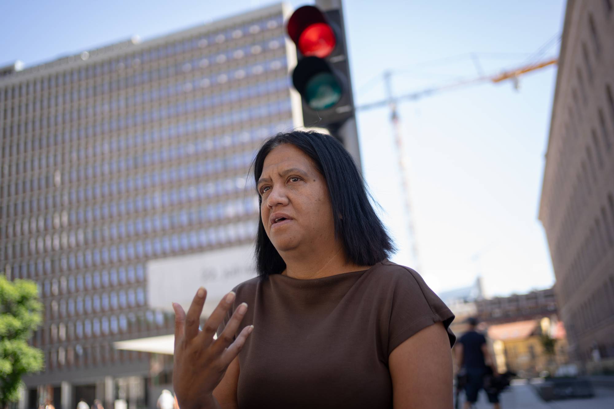 Kvinne med mørkt hår gestikulerer foran Høyblokka i Oslo sentrum. (Bildebeskrivelsen er laget av en KI-tjeneste)