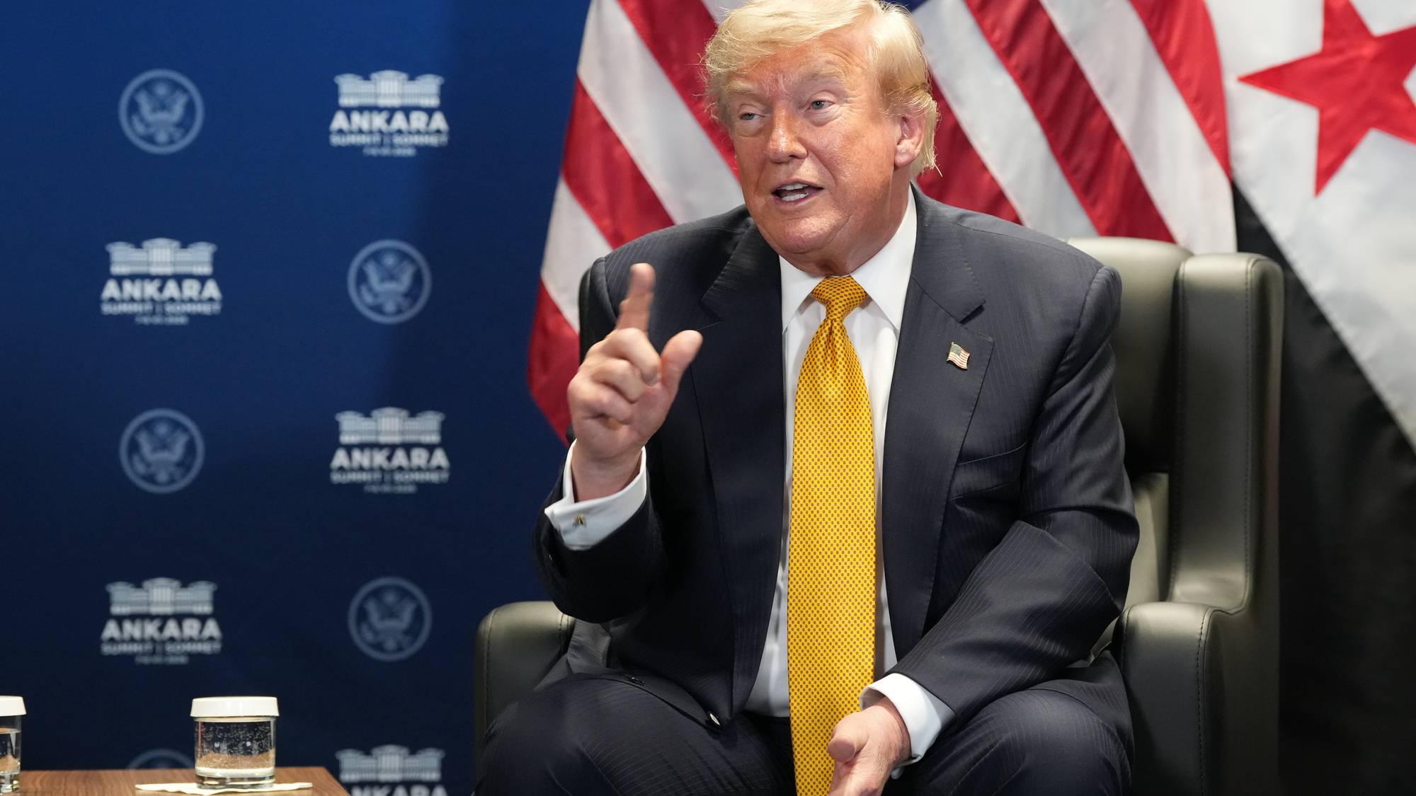 Donald Trump sitter i en stol og snakker foran amerikanske flagg og Ankara-skilt. (Bildebeskrivelsen er laget av en KI-tjeneste)