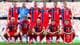 Foto: Vegard Grøtt / NFF Norges herrelandslag i fotball poserer før en kamp. Spillerne er kledd i røde drakter med blått og hvitt design. Bak spillerne sitter tilskuere på tribunen. (Bildebeskrivelsen er laget av en KI-tjeneste)