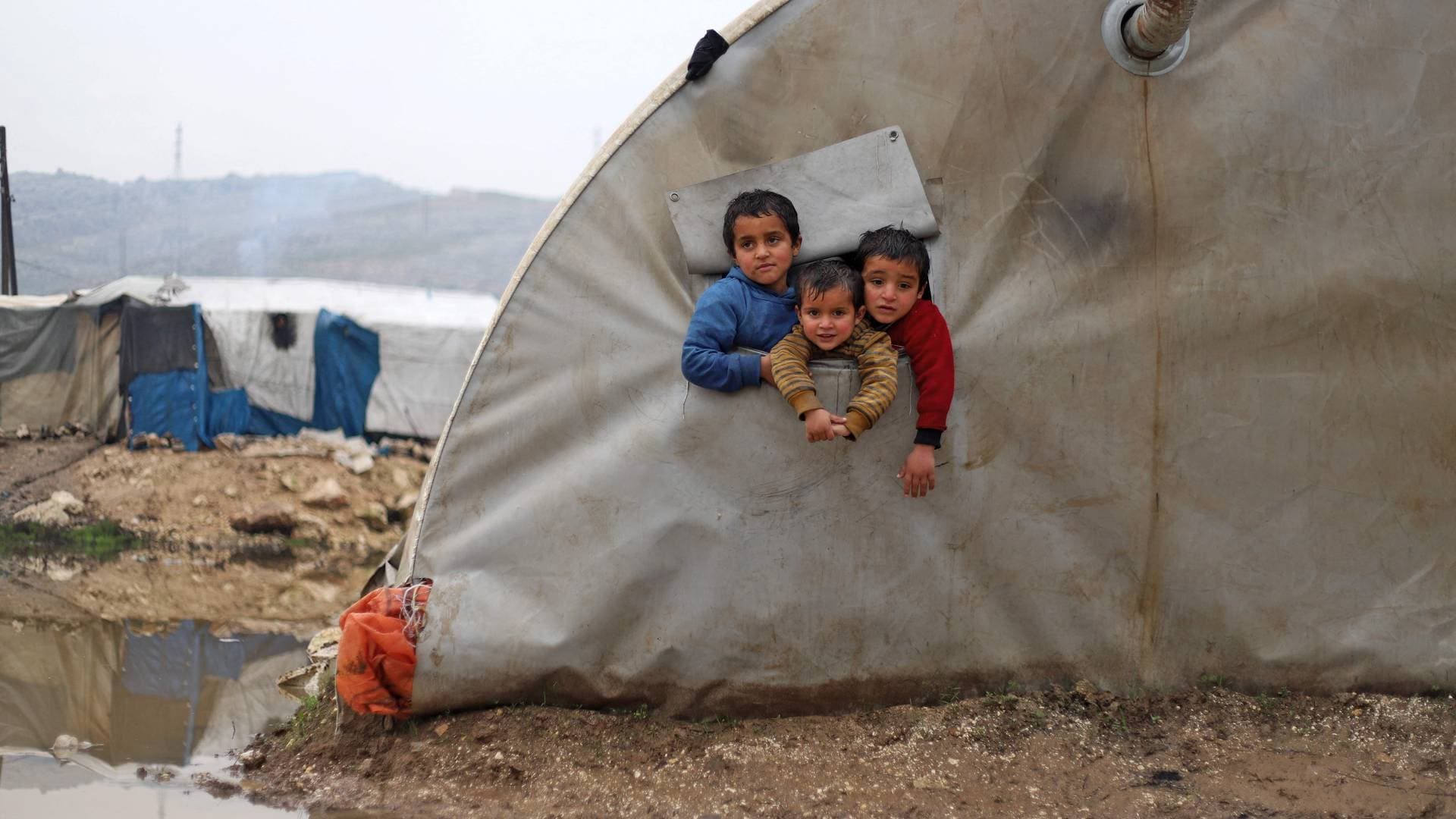 Syrian children look out of their ​tent as heavy rain floods the al-Balea camp for⁢ internally displaced persons near the town of jisr al-Shughur in Syria's northwestern ‌Idlib province on January 13, 2022