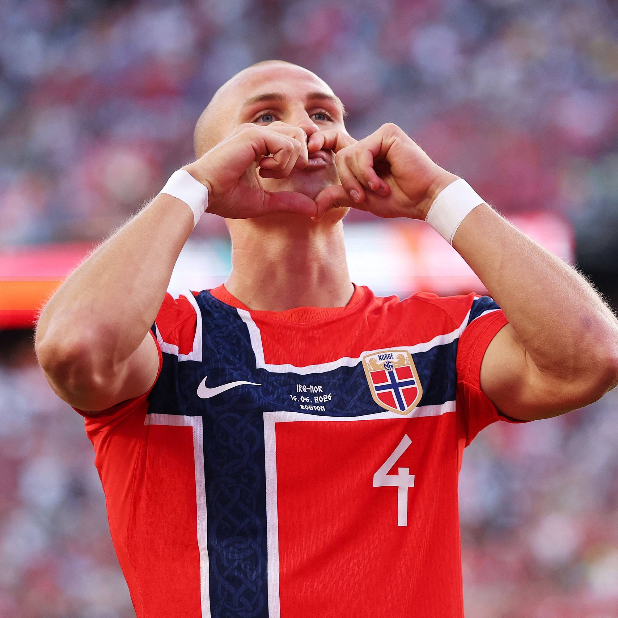 En fotballspiller i Norge-drakt lager hjertesymbol med hendene. Spilleren har nummer fire på drakten. Bakgrunnen viser en fullsatt tribune. (Bildebeskrivelsen er laget av en KI-tjeneste)
