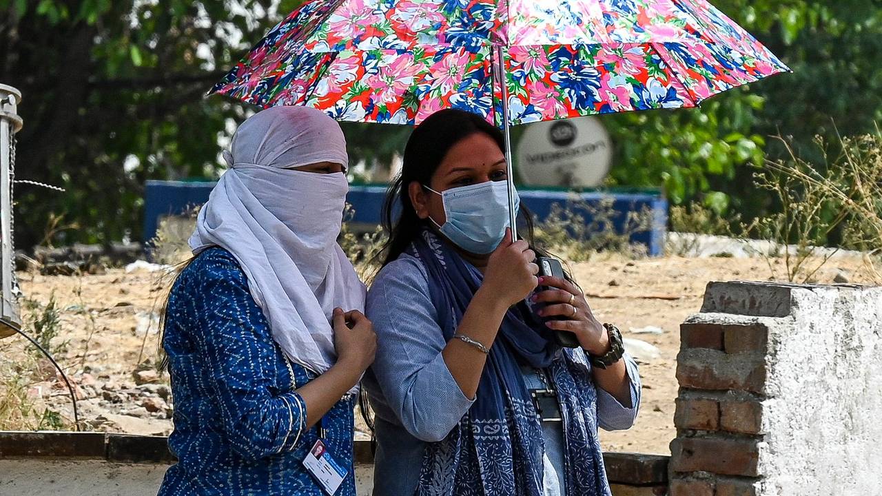 Girls use an umbrella to take shelter from heat on a hot summer afternoon in New Delhi on April 28, 2022. (Photo by Prakash SINGH / AFP)