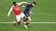 ATTILA KISBENEDEK / AFP,NTB Two football players in opposing team jerseys contest a ball on a green pitch. The player in the red and white Arsenal jersey is actively tackling the player in the dark blue Paris Saint-Germain jersey. The PSG player appears to be injured, with visible blood on his shin. A football rests nearby on the grass, with a white line marking the edge of the pitch. (Bildebeskrivelsen er laget av en KI-tjeneste)